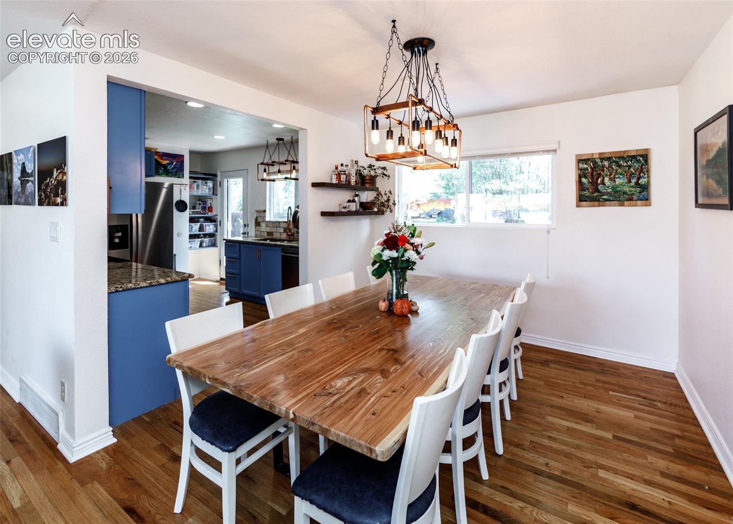Wood-finish flooring throughout, with a framed opening leading to a kitchen featuring blue cabinetry and stainless steel appliances