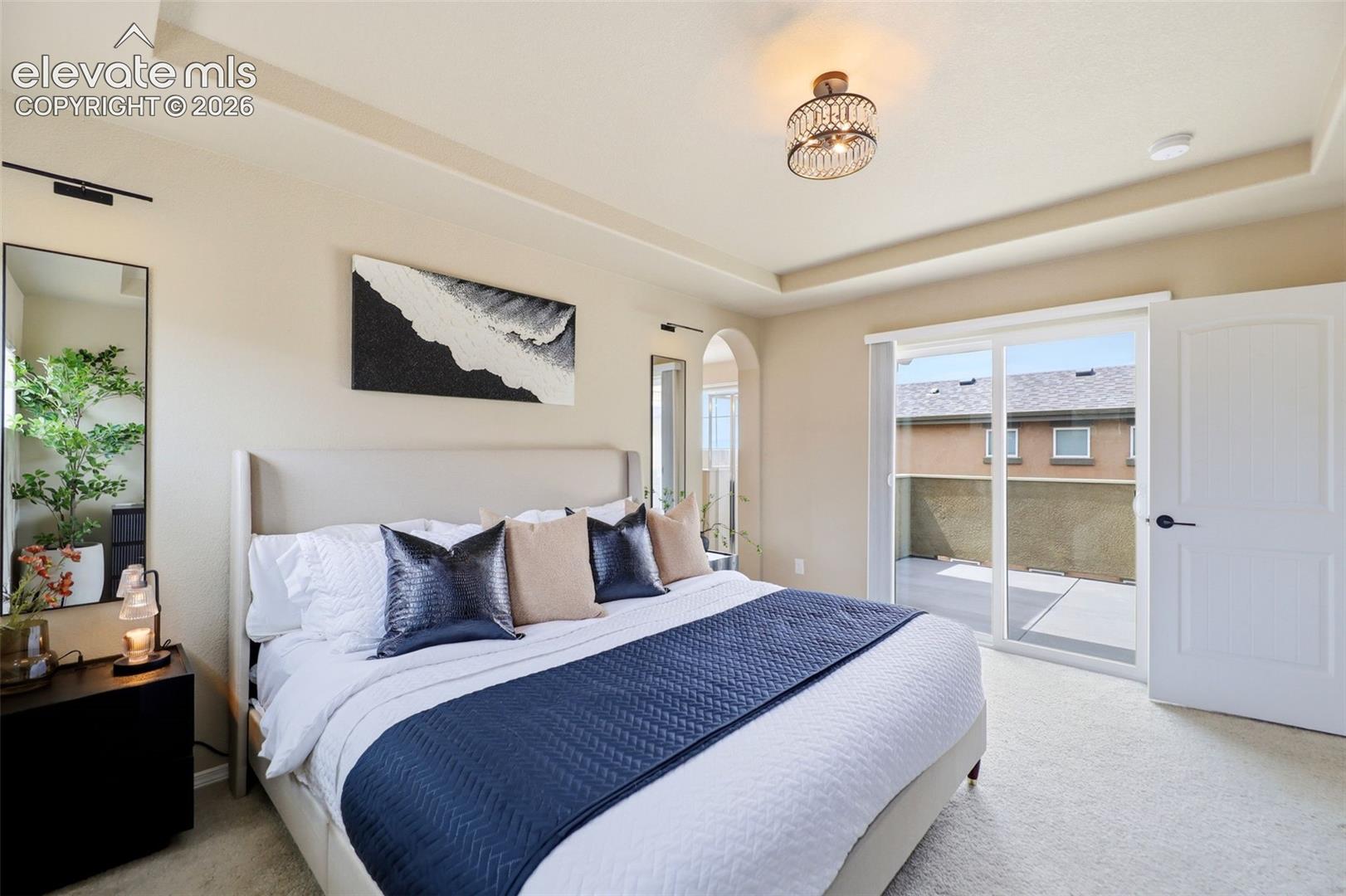 Tray ceiling, carpeted flooring, arched doorway, sliding glass door leading out to the balcony.