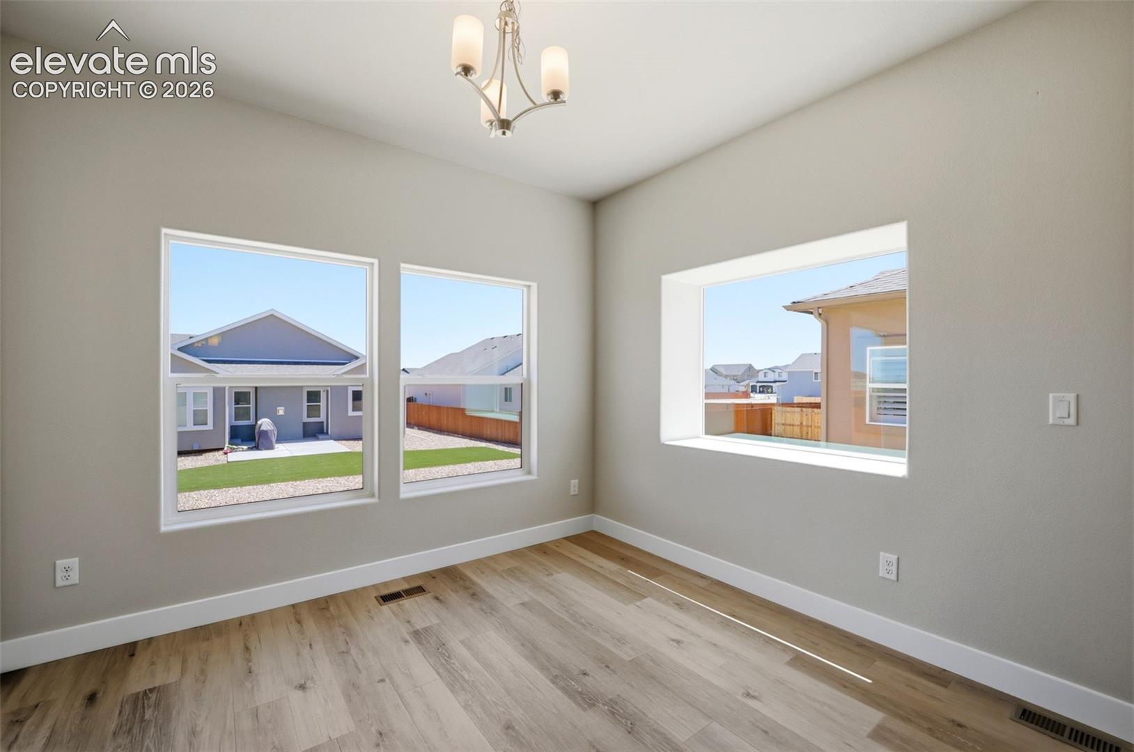Neutral-toned interior featuring wood-finish flooring, three large windows, and a multi-arm pendant light fixture