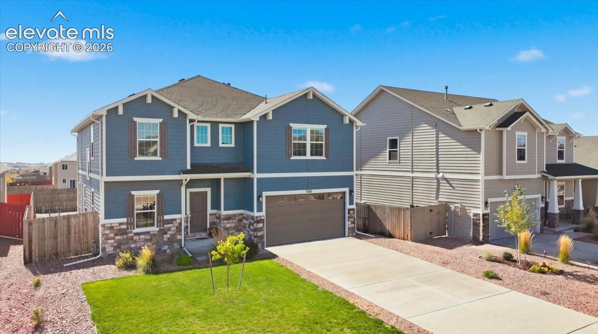 Two-story exterior featuring blue horizontal siding, stone veneer accents, multi-pane windows with shutters, a concrete driveway, and an attached two-car garage