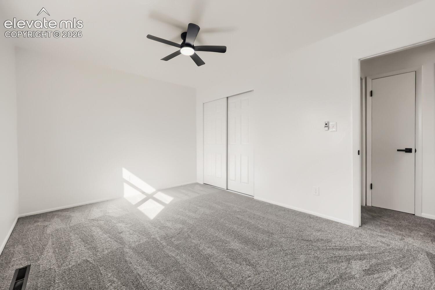 Wall-to-wall carpeting, white walls, black ceiling fan, white sliding closet doors, and a white interior door with black hardware