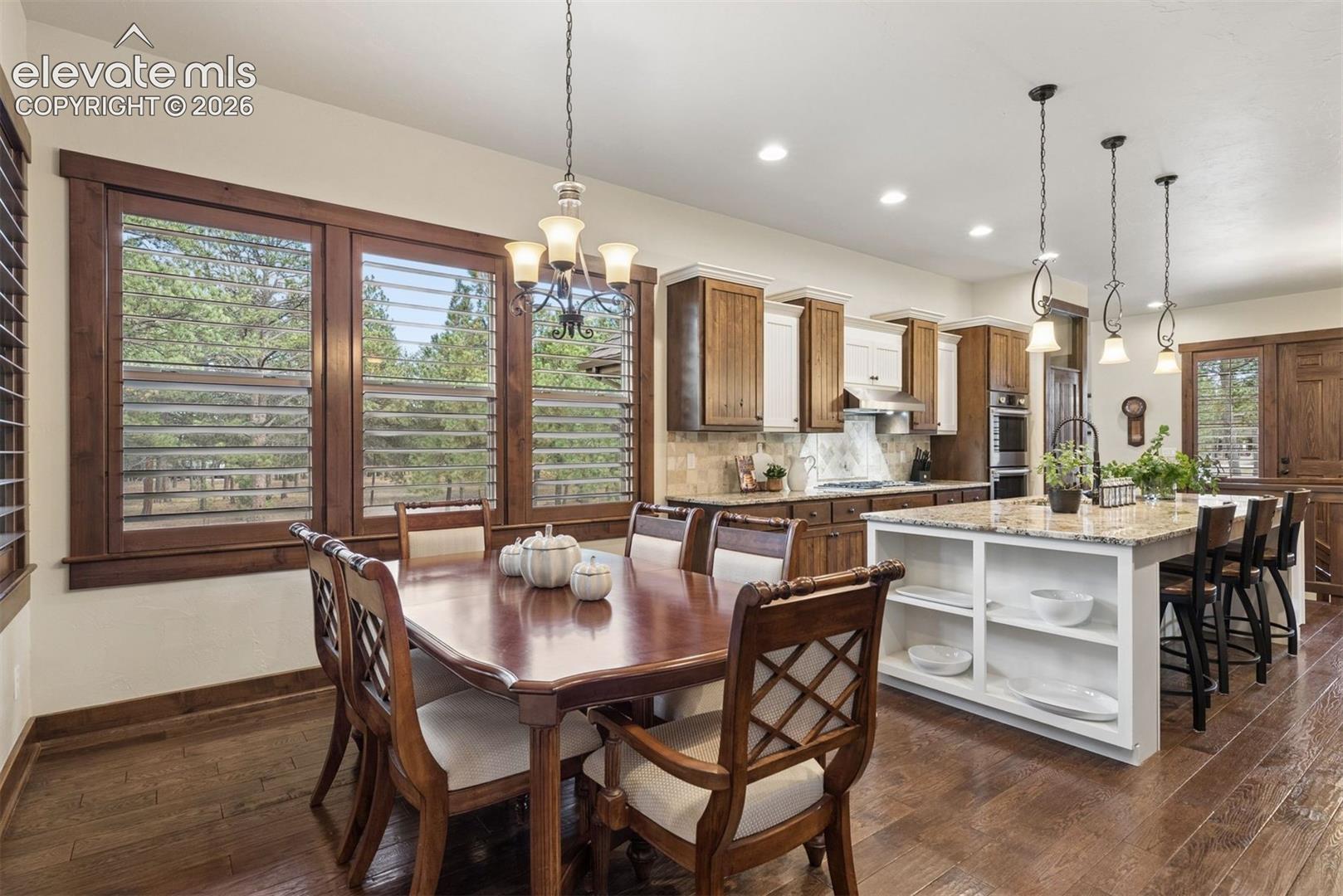 Kitchen featuring custom cabinetry, stone-surfaced center island with built-in shelving, wood-finish flooring, and natural lighting provided by large windows with wood trim