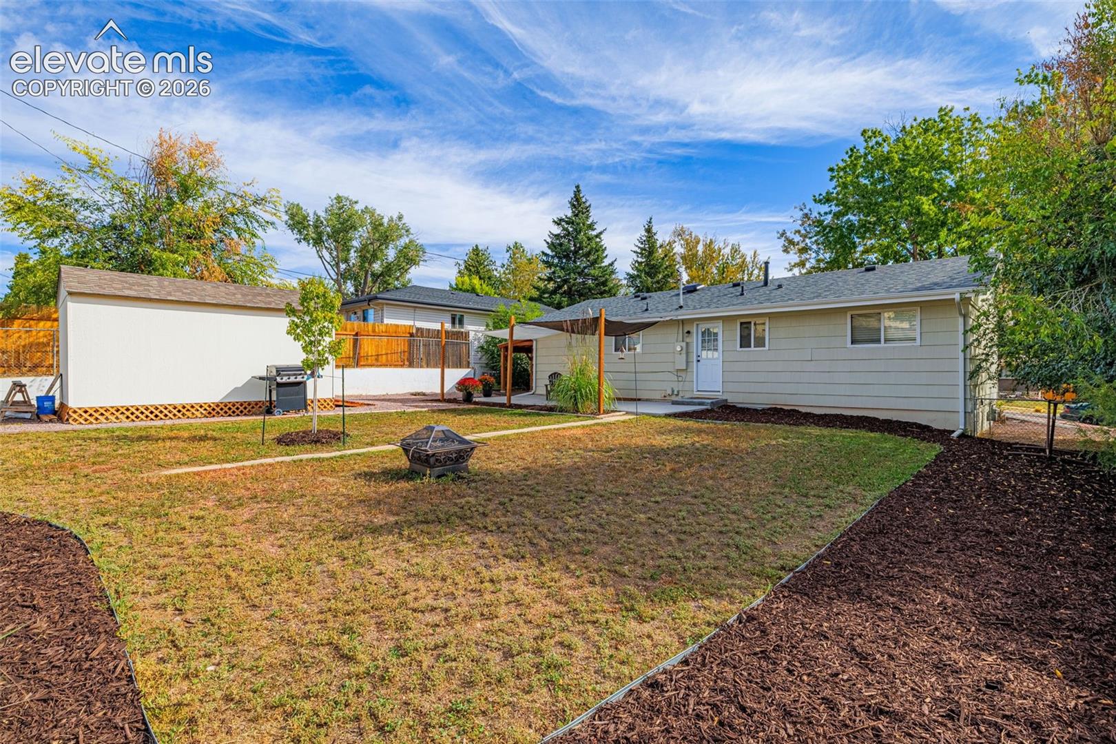 Expansive backyard featuring a dedicated fire pit area, a storage shed, and a shaded concrete patio