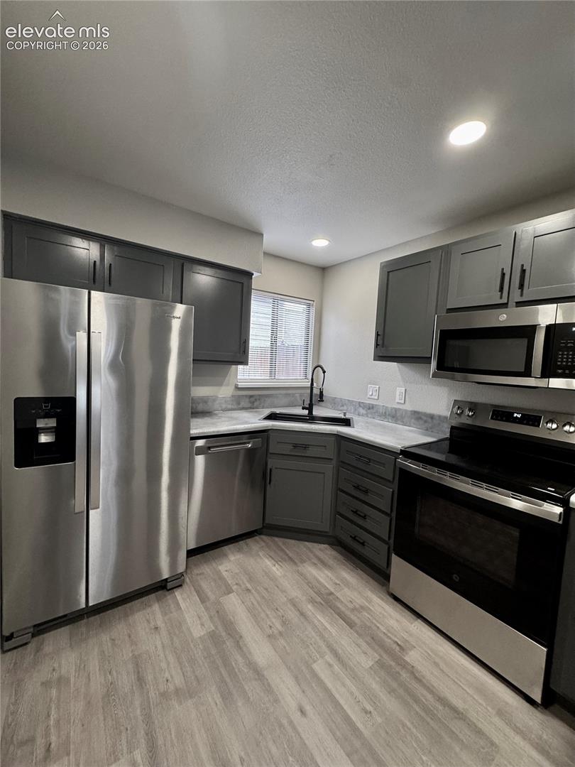 Kitchen featuring stainless steel appliances, grey cabinetry, light-toned countertops, wood-finish flooring, and recessed lighting