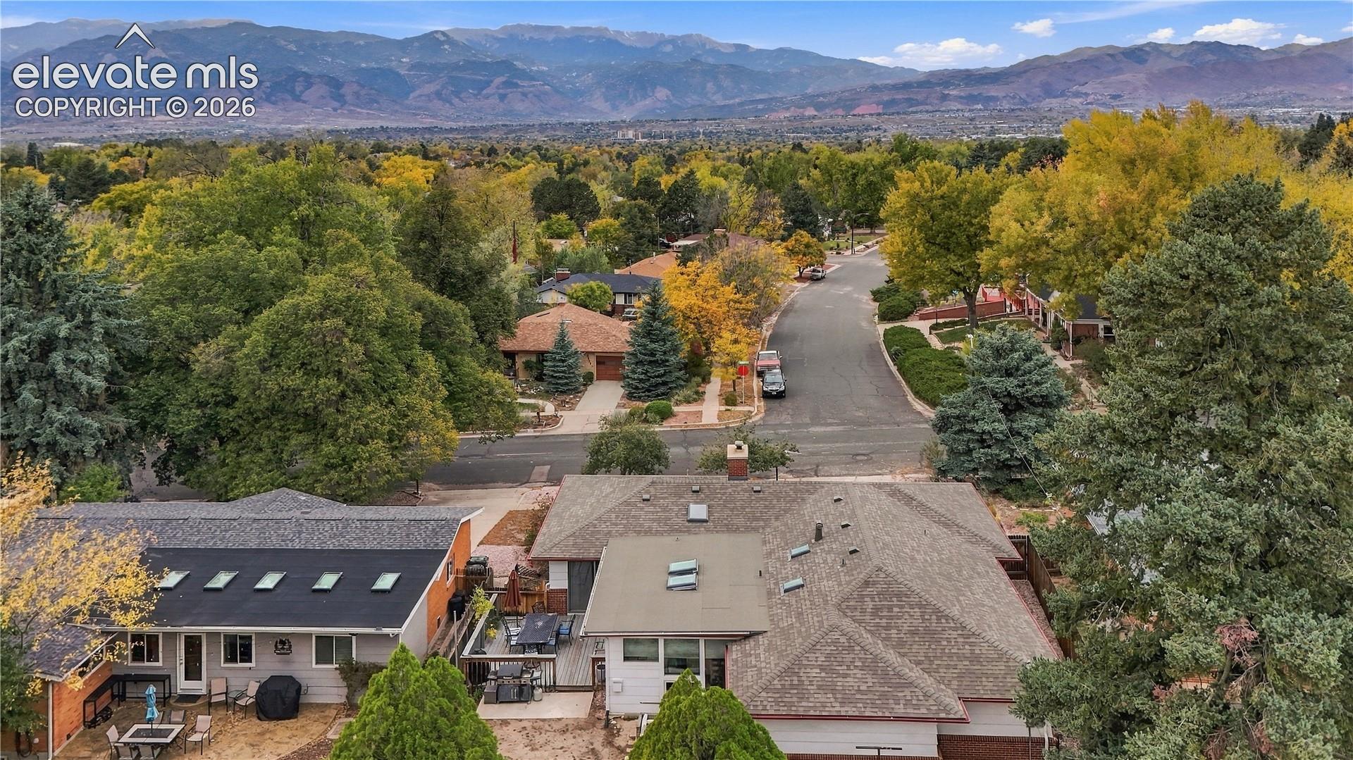 Aerial perspective showcasing mature tree canopy, asphalt shingle roofing, multiple skylights, and expansive mountain scenery