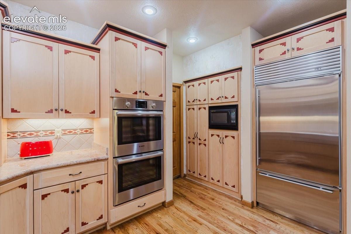 Kitchen featuring light-toned cabinetry with decorative accents, stainless steel double wall ovens, a built-in microwave, and a large stainless steel refrigerator