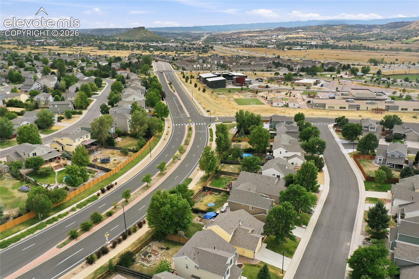 Aerial perspective of a residential community featuring multi-level dwellings, suburban street infrastructure, established landscaping, and distant mountain topography