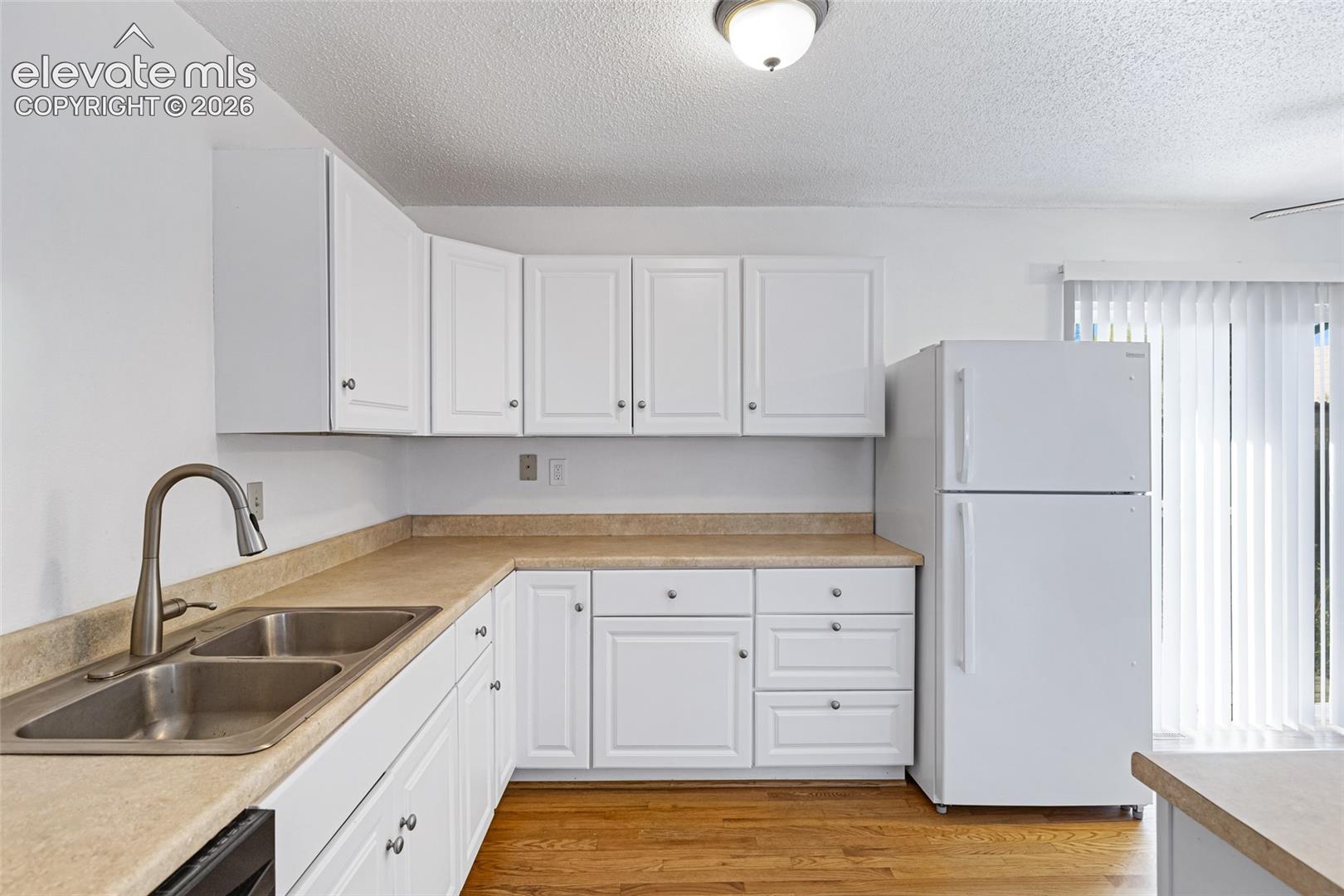 Kitchen featuring white cabinetry, light countertops, a stainless steel double-basin sink with a gooseneck faucet, and wood-finish flooring