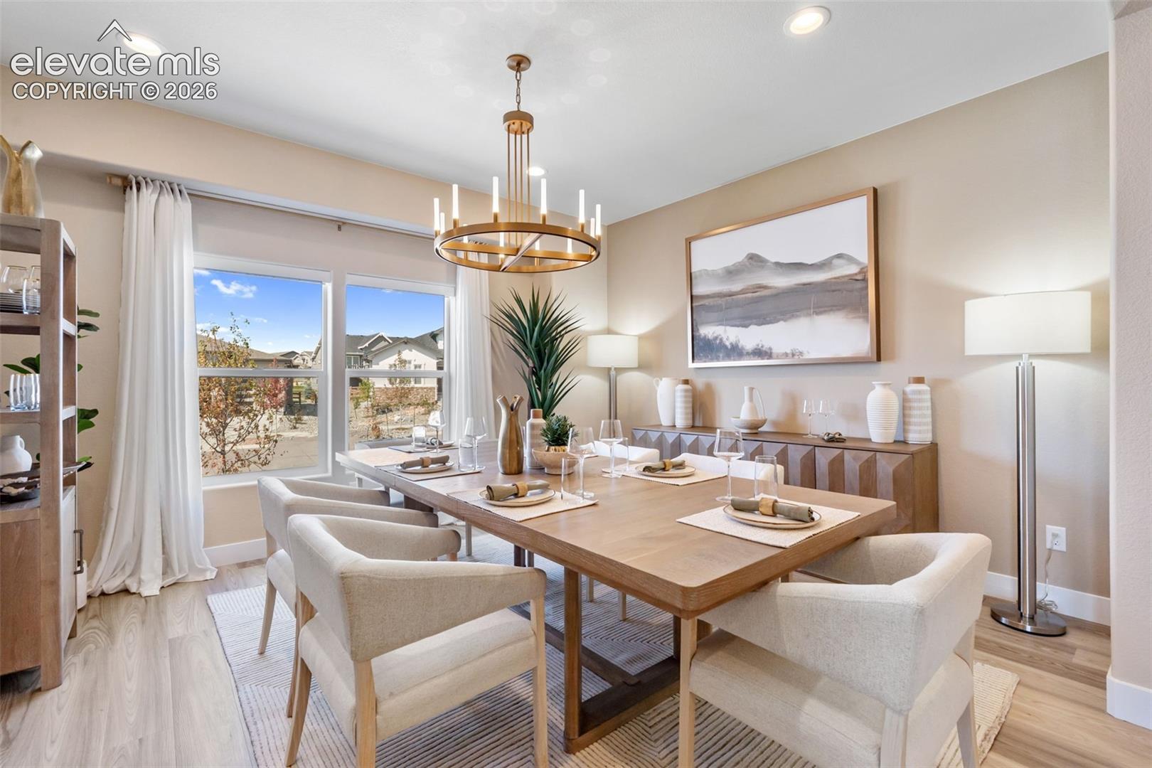 Dining area featuring light wood-finish flooring, recessed ceiling lighting, and a prominent multi-tiered gold-tone metal chandelier
