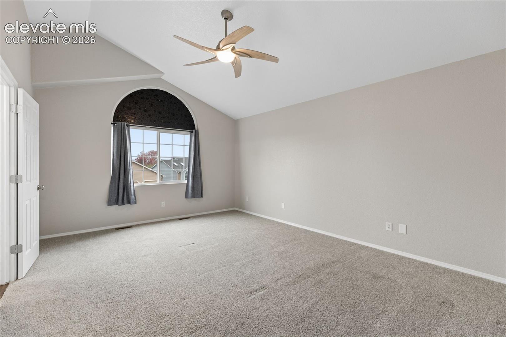 Vaulted ceiling featuring an arched window, neutral wall palette, and a multi-blade ceiling fan with integrated lighting