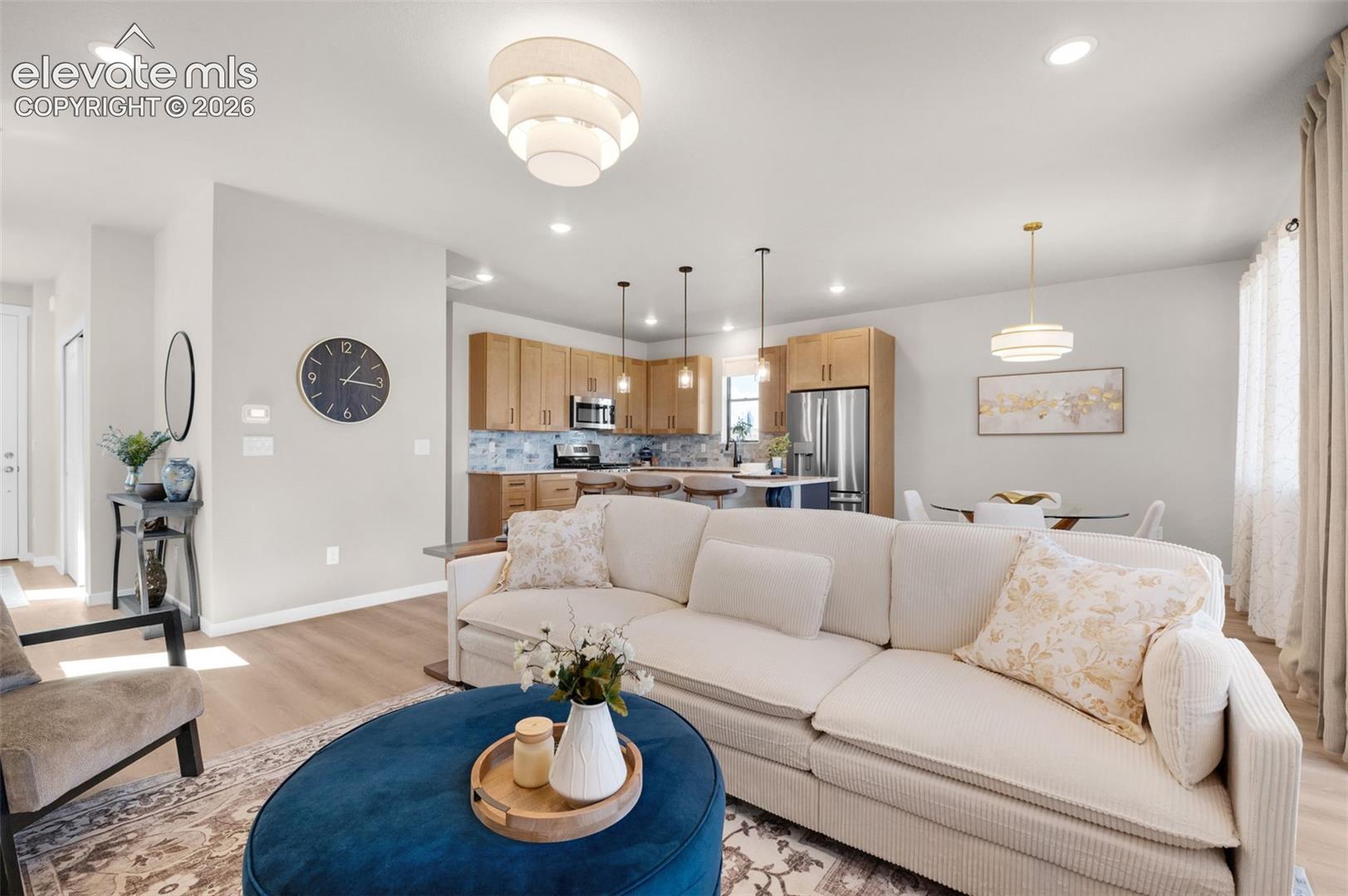 Open-concept living area featuring light wood-finish flooring, recessed lighting, and a modern tiered chandelier