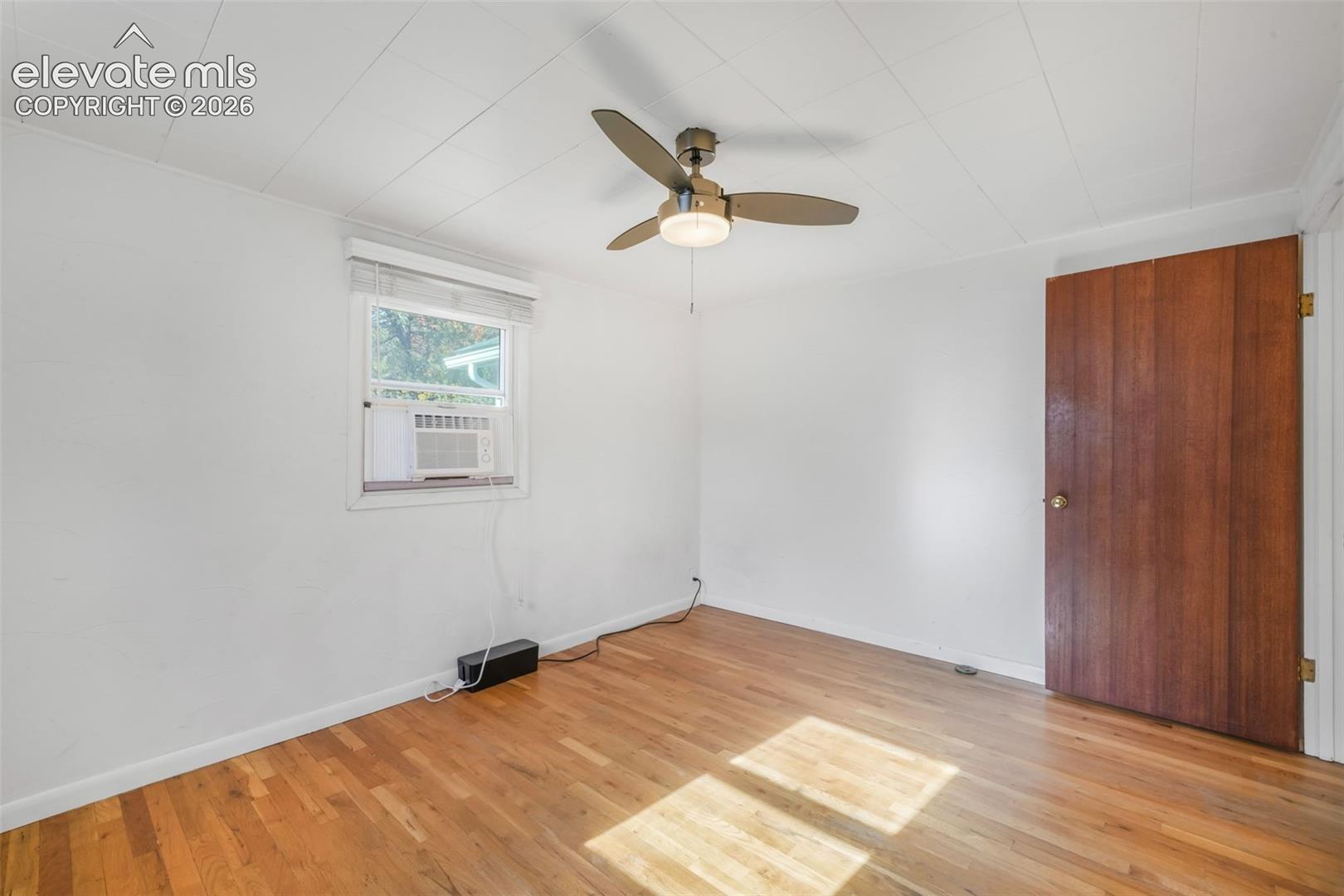 Wood-finish flooring, white painted walls, and a ceiling-mounted fan with integrated lighting