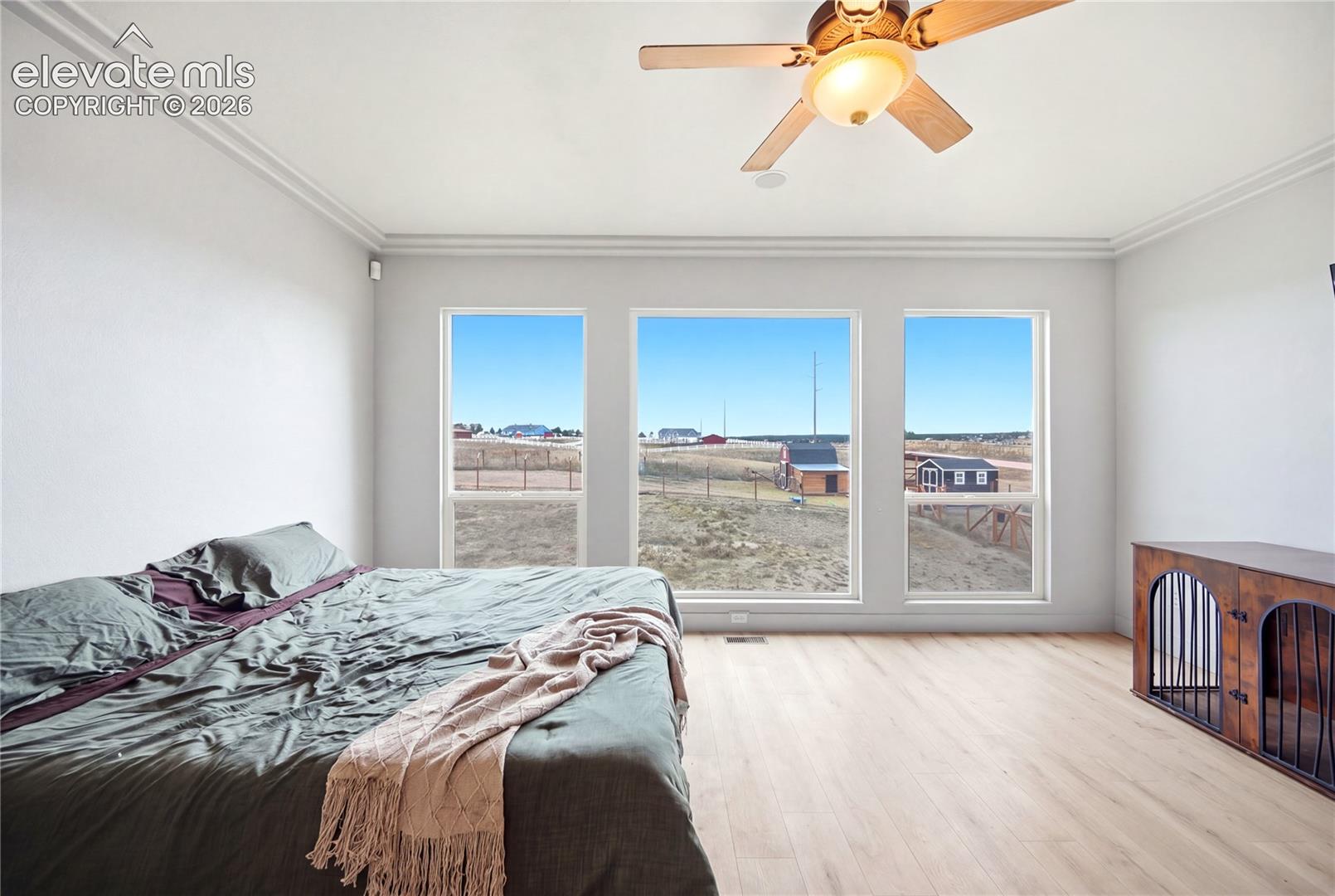 Neutral-toned interior featuring wood-finish flooring, triple-pane windows, crown molding, and a ceiling-mounted light fixture with fan