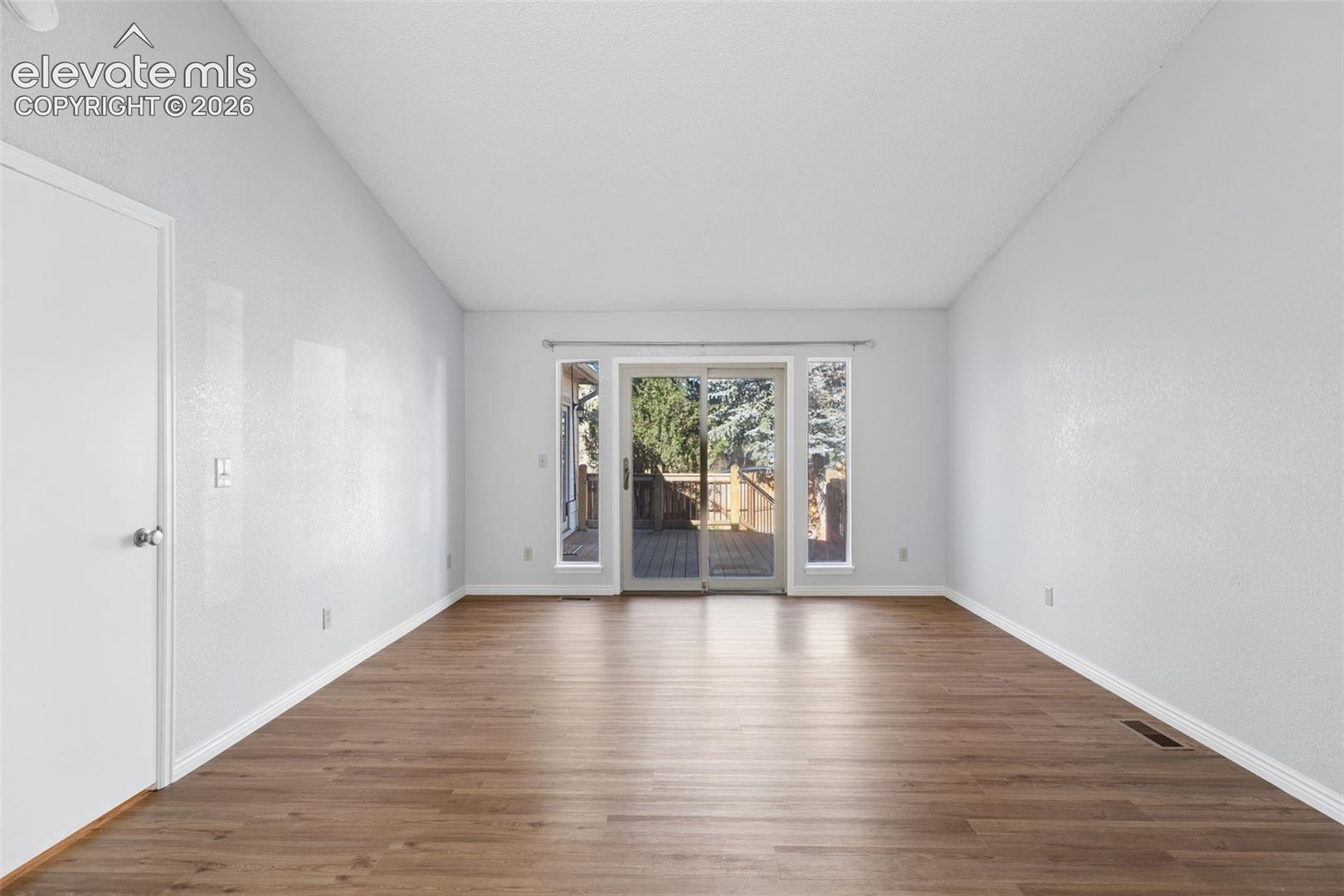 Vaulted ceilings featuring wood-finish flooring, neutral wall paint, and a sliding glass door with flanking windows