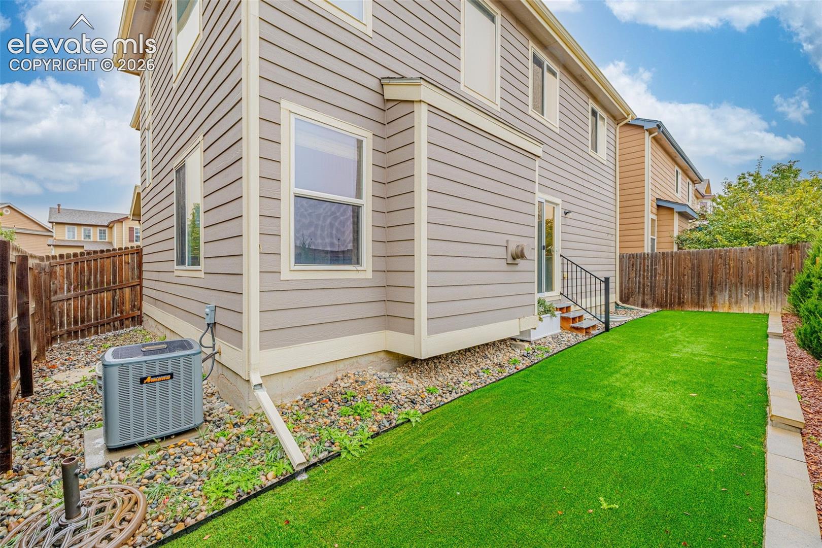 Two-story horizontal lap siding exterior featuring a grass lawn, metal stair railing, and rock ground cover