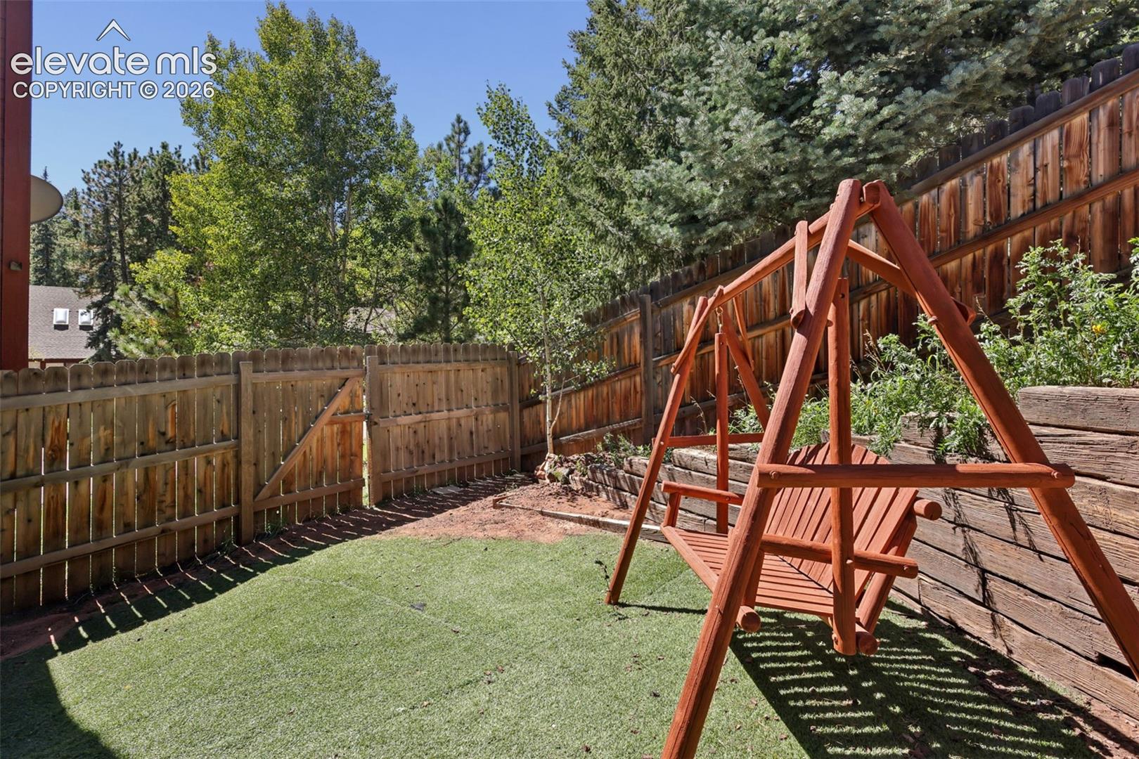 Fenced backyard featuring artificial turf, a wood fence, and a wood swing
