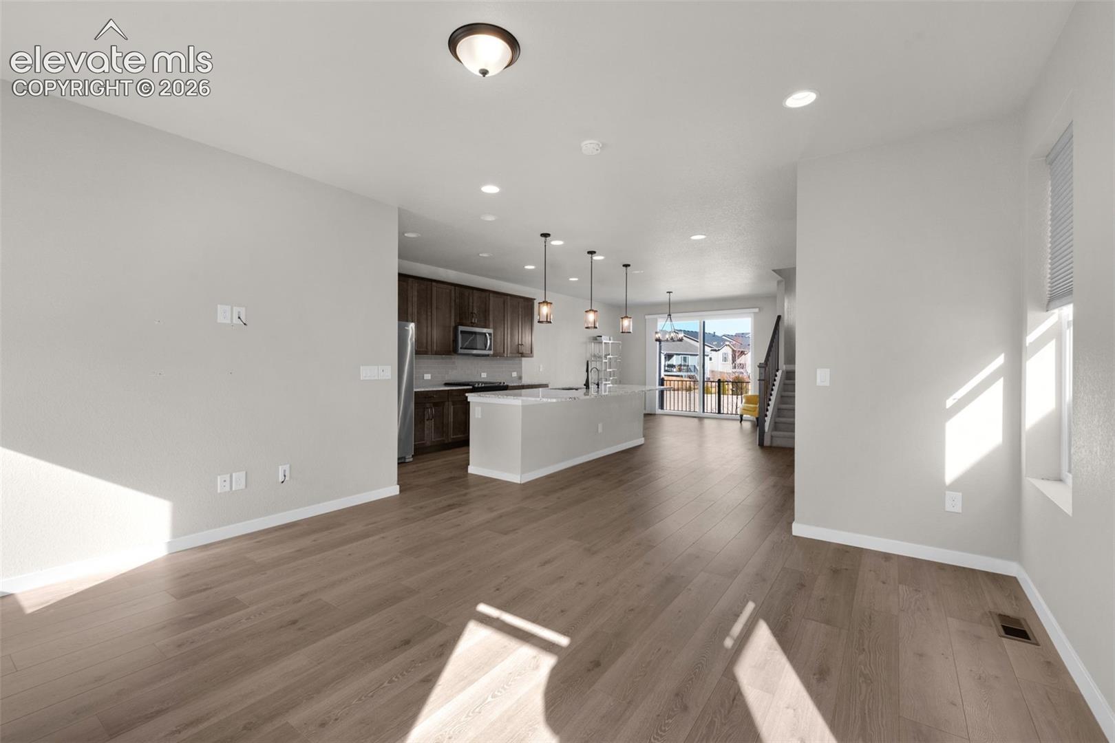 Open-concept interior featuring wood-finish flooring, a kitchen island with pendant lighting, stainless steel appliances, and recessed lighting