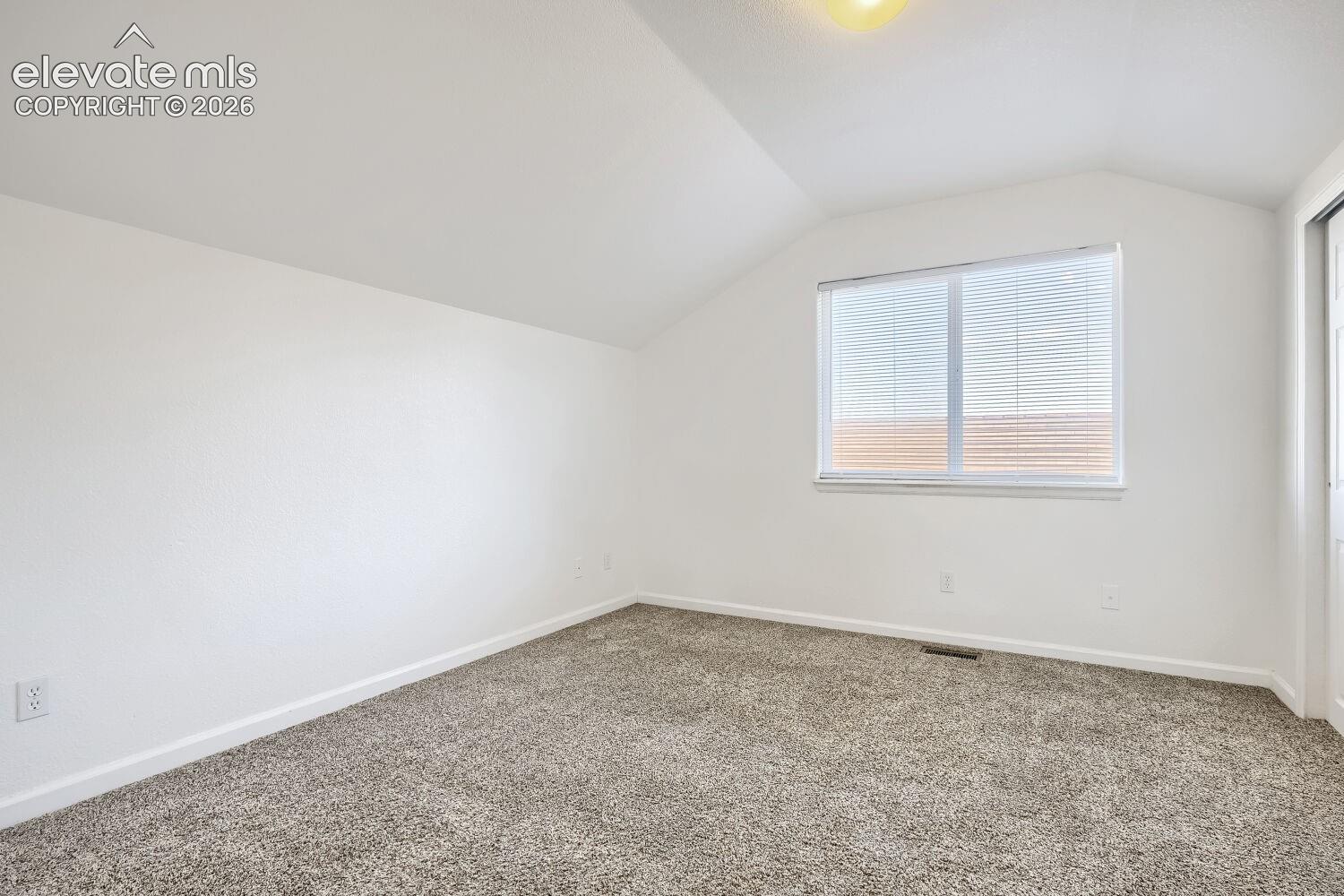 Neutral interior space featuring vaulted ceilings, wall-to-wall carpeting, and a single-pane window