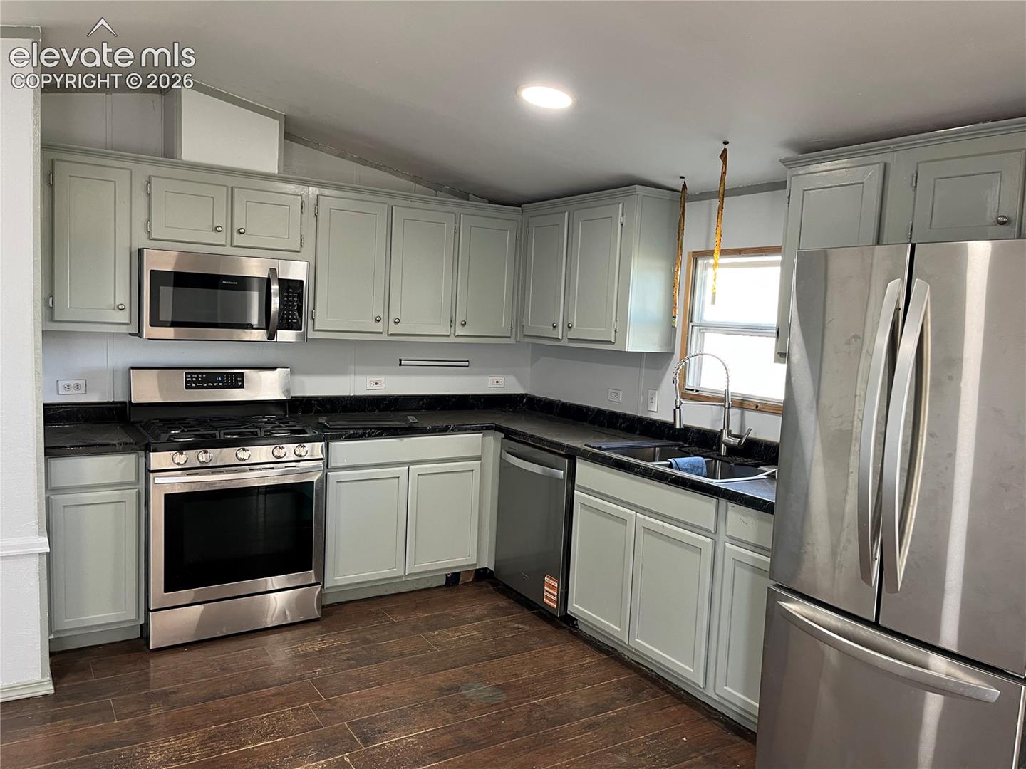 Kitchen with wood-finish flooring, light-toned cabinetry, stainless steel appliances, dark countertops, and a full tile backsplash