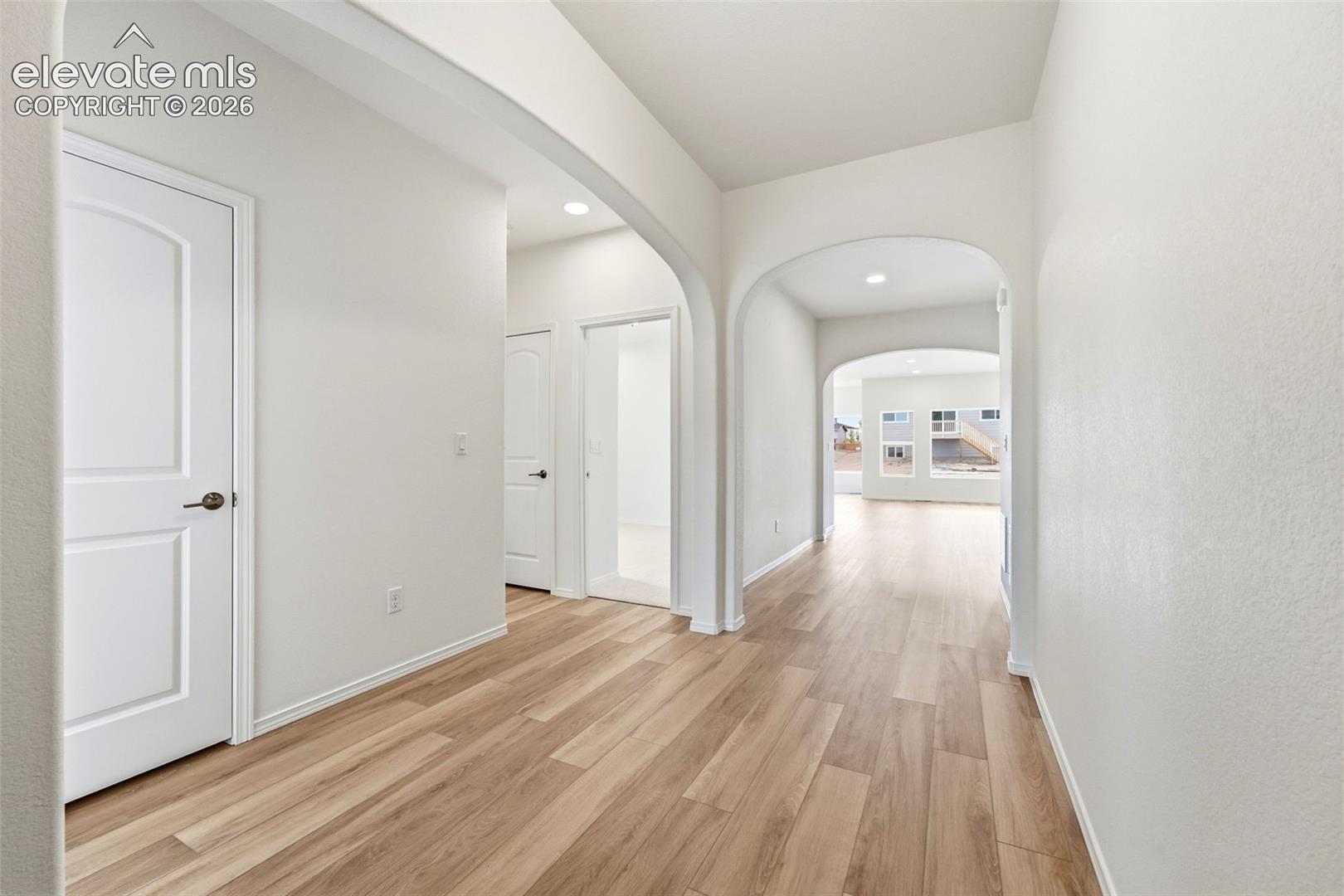 Interior hallway featuring arched architectural pass-throughs, wood-finish flooring, recessed lighting, and multi-panel doors