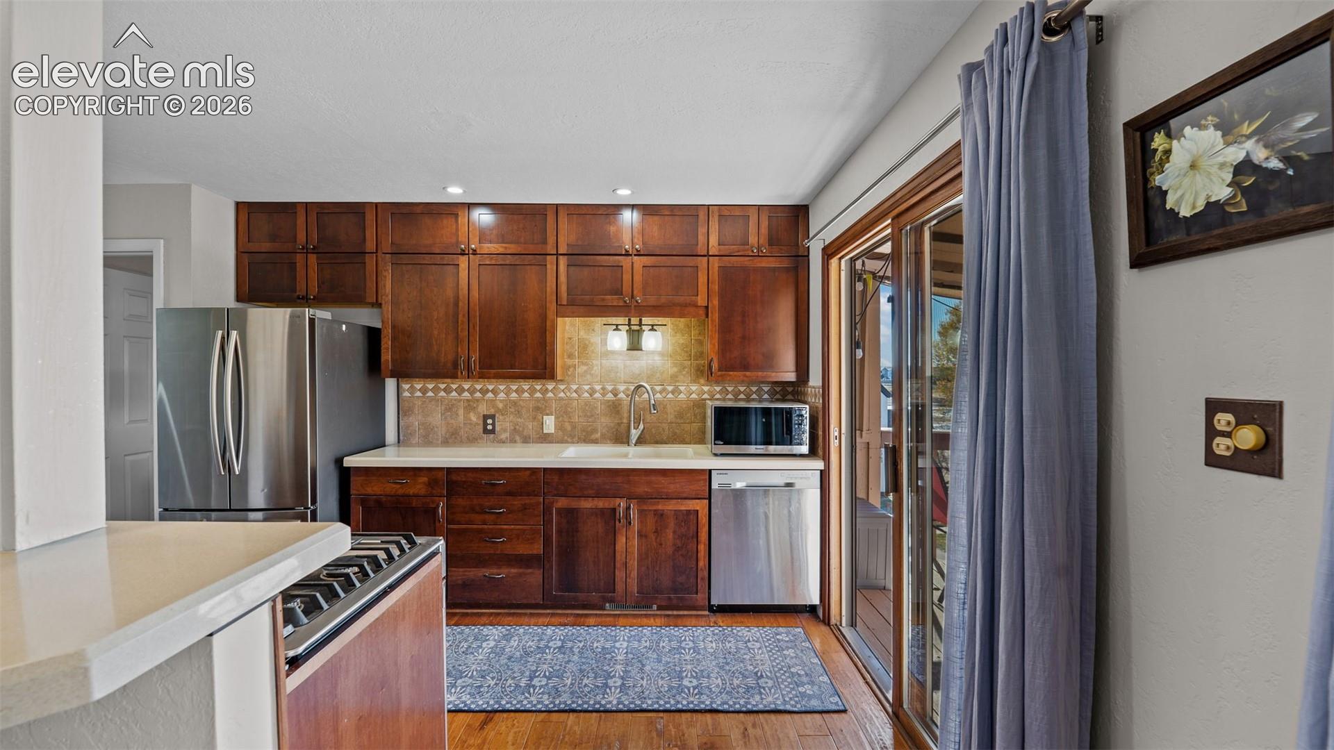 Kitchen featuring stained wood cabinetry, tile backsplash, stainless steel appliances, and a sliding glass door
