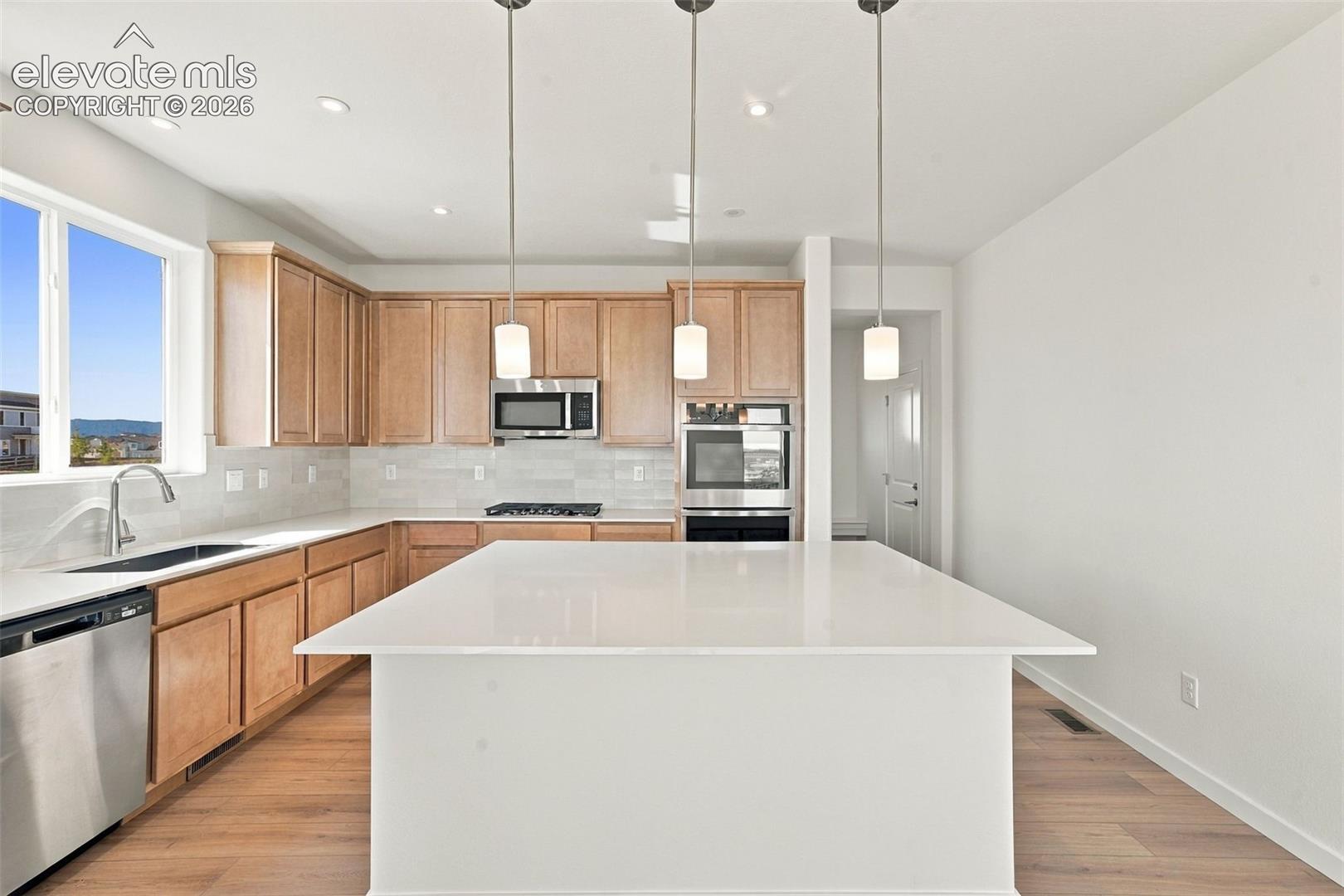 Kitchen featuring a large island, wood-finish flooring, stainless steel appliances, light-toned cabinetry, and pendant lighting