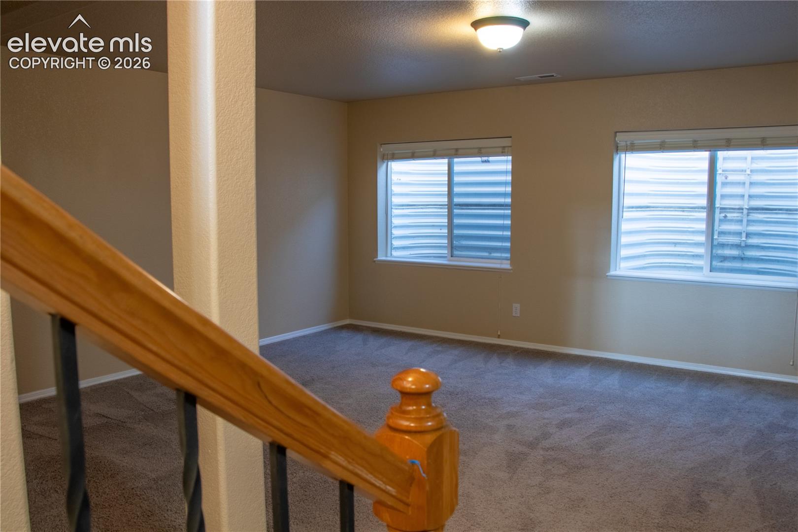 Carpeted room featuring two windows with horizontal blinds, light beige walls, and a ceiling-mounted light fixture