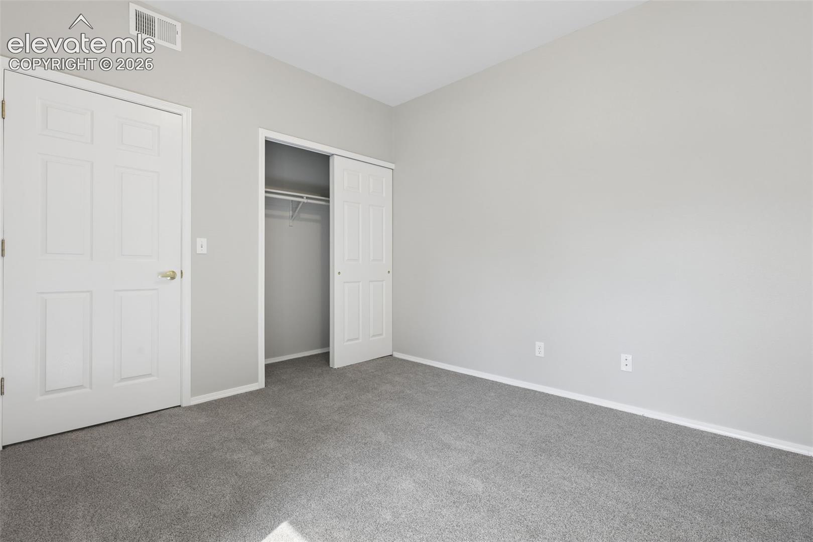 Wall-to-wall carpeting, light gray wall paint, white trim, and a bi-fold closet with wire shelving