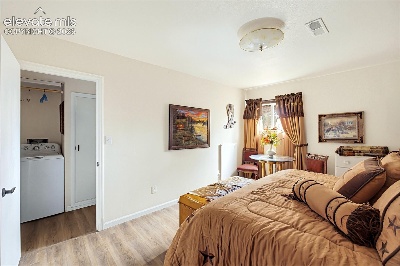 Interior room featuring wood-finish flooring, a wall-mounted heater, and an attached laundry area with interior closet space