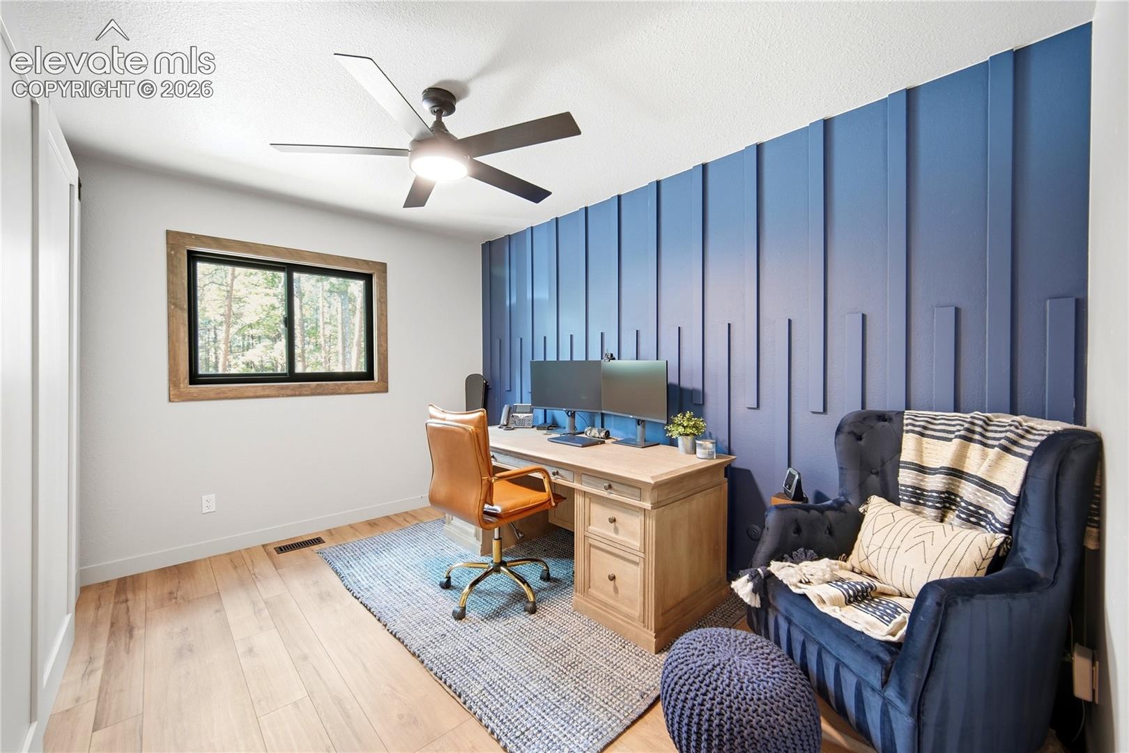 Room featuring wood-finish flooring, a blue vertical slat accent wall, and a ceiling fan with integrated lighting