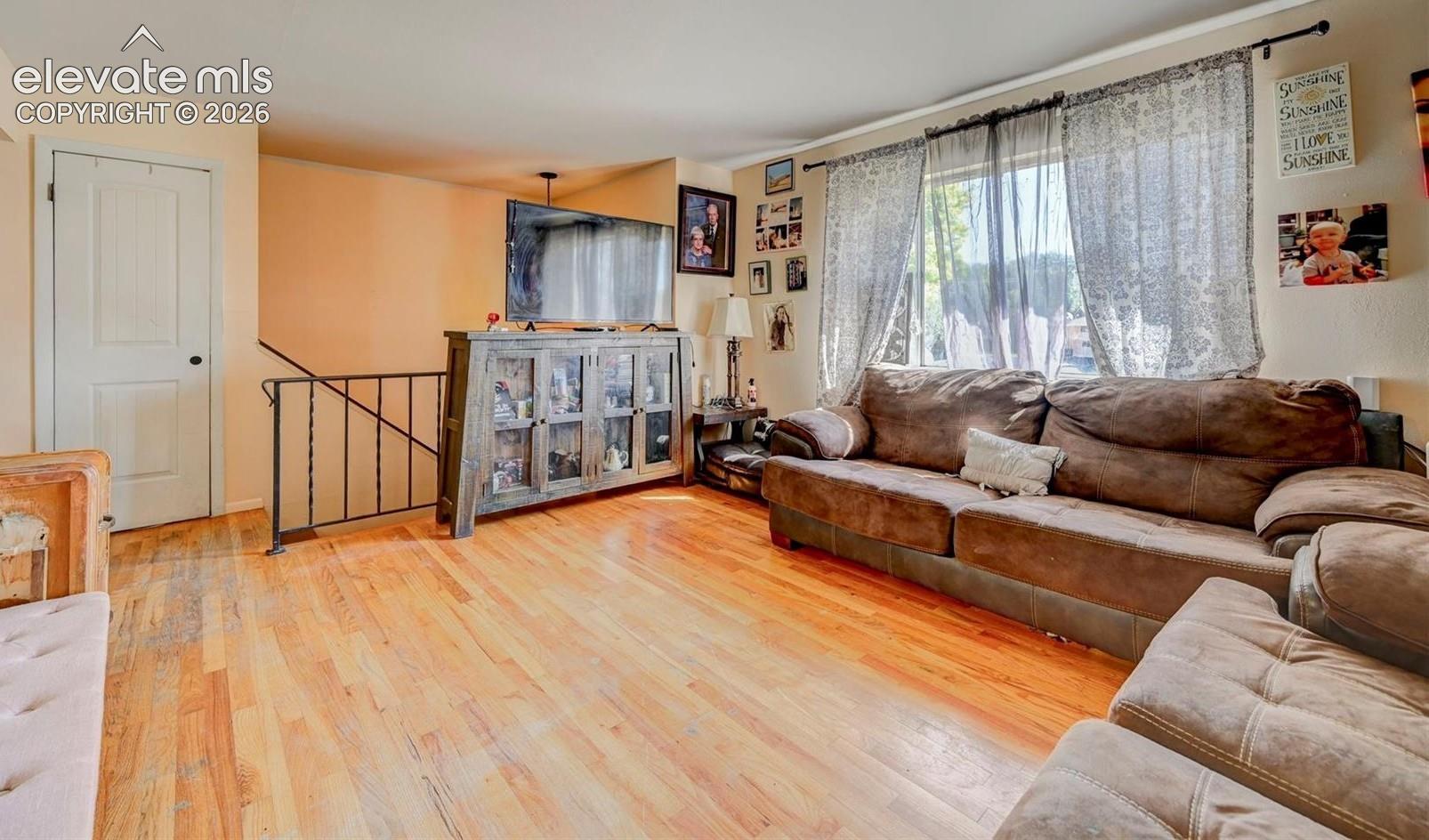 Living space featuring wood-finish flooring, a large window with natural light, a white paneled door, and a metal-railed staircase