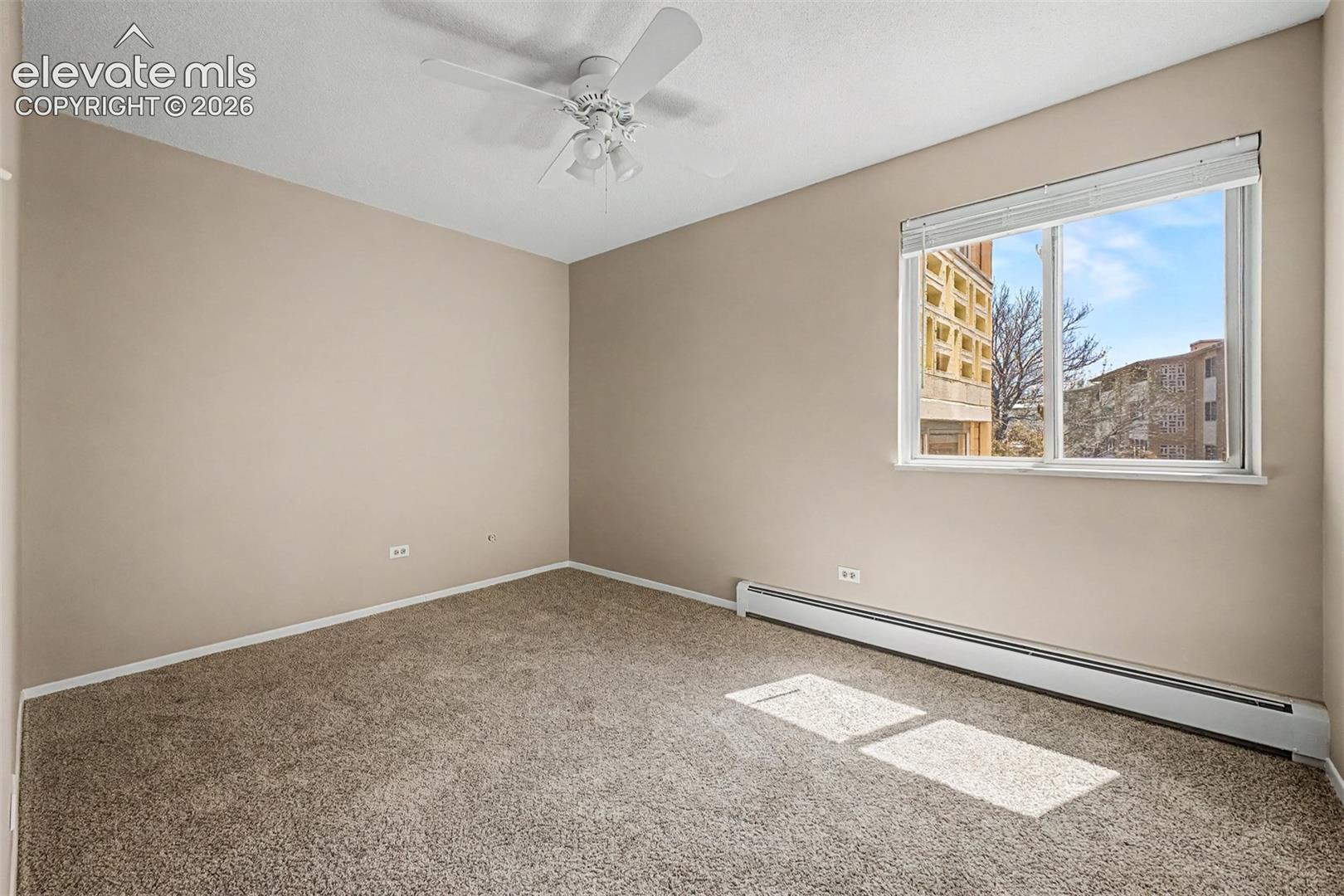 Carpeted room featuring a ceiling fan, baseboard heating, a large window, and light-toned walls