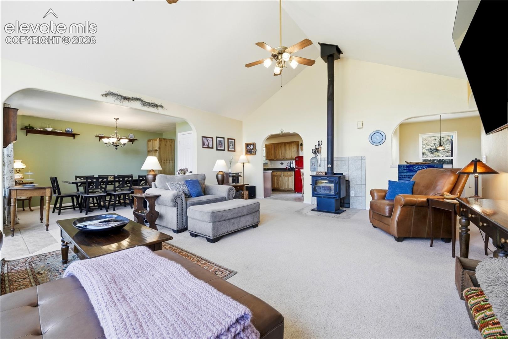 Vaulted ceiling, ceiling fan, wood-burning stove with tile surround, arched doorways, and recessed lighting