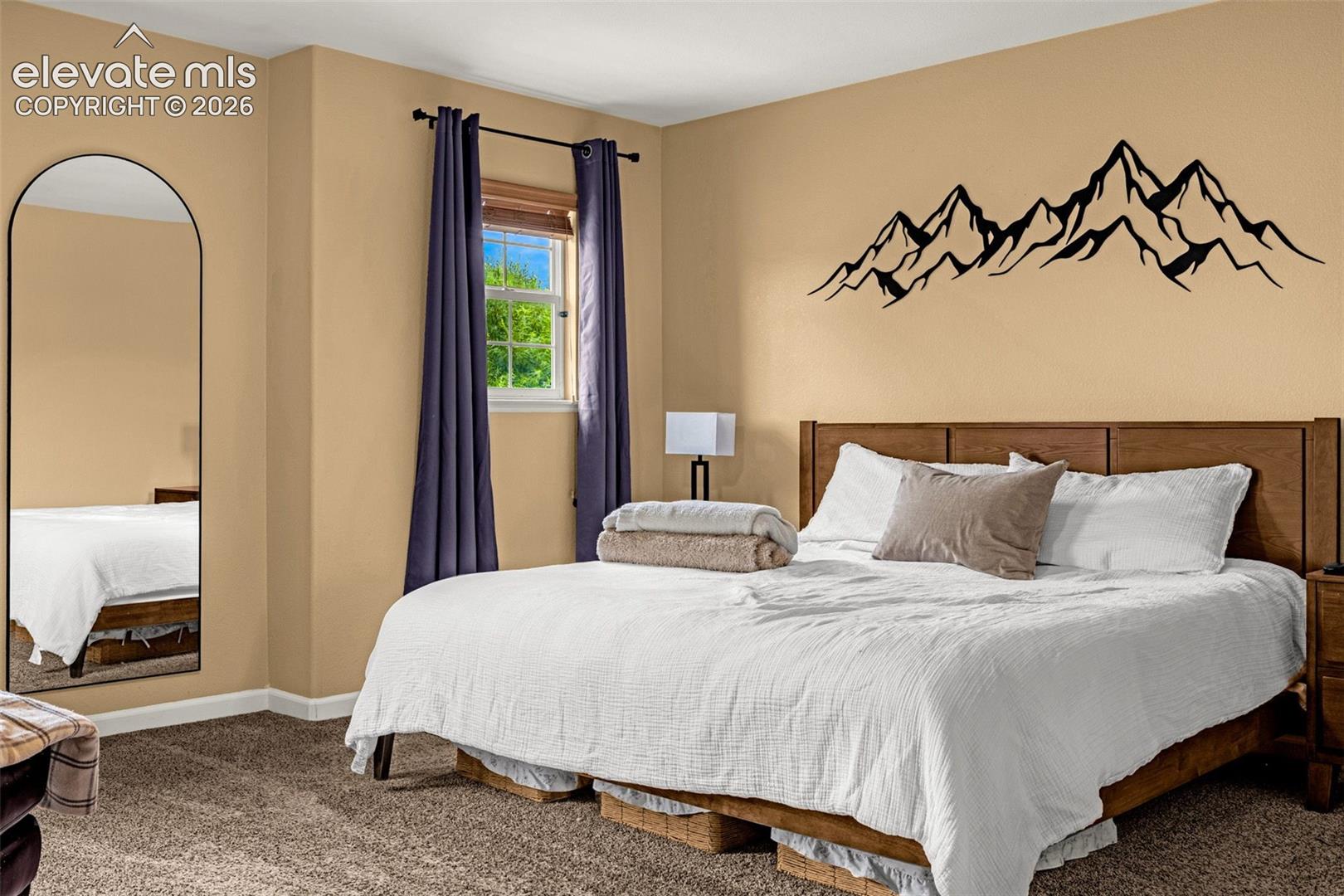 Neutral-toned room featuring wall-to-wall carpeting, a multi-pane window with a wood-finish frame, and a tall, arched floor mirror