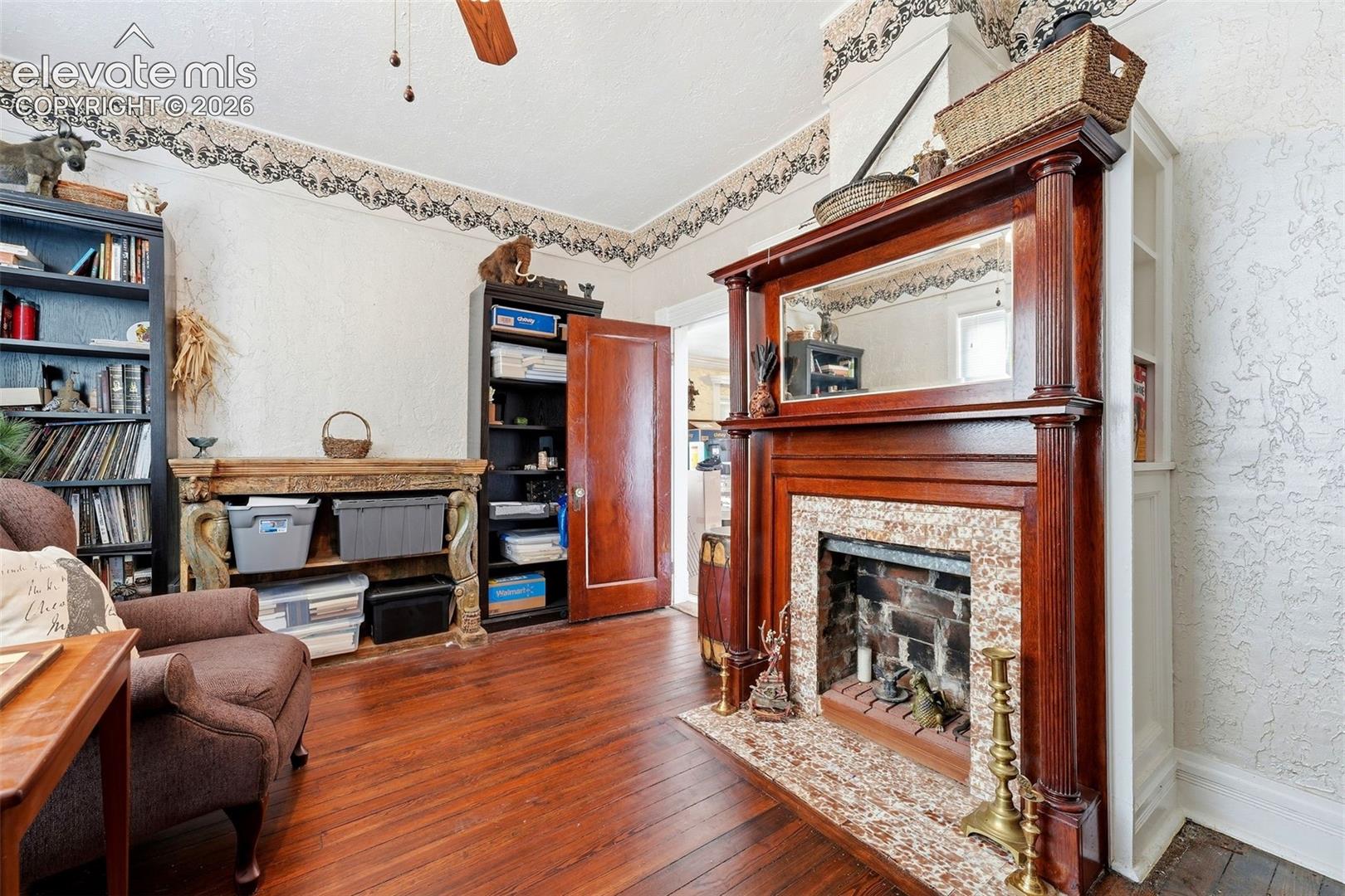 Wood-finish flooring, built-in shelving, wood door, and a fireplace with a decorative mantel and hearth