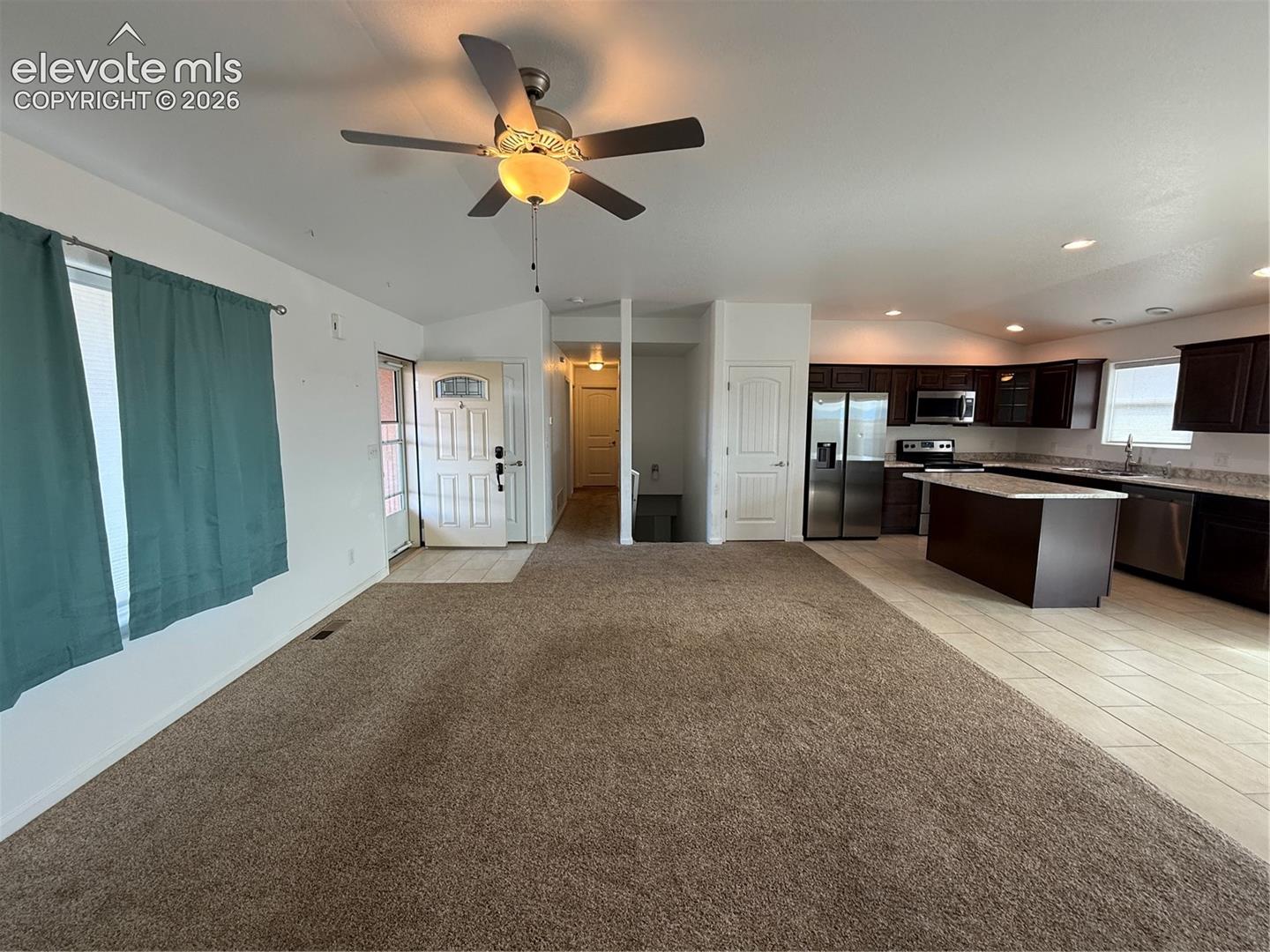 Open-concept interior featuring vaulted ceilings with a central paddle fan, a kitchen island with a stone-surface countertop, dark wood-finish cabinetry, and recessed lighting