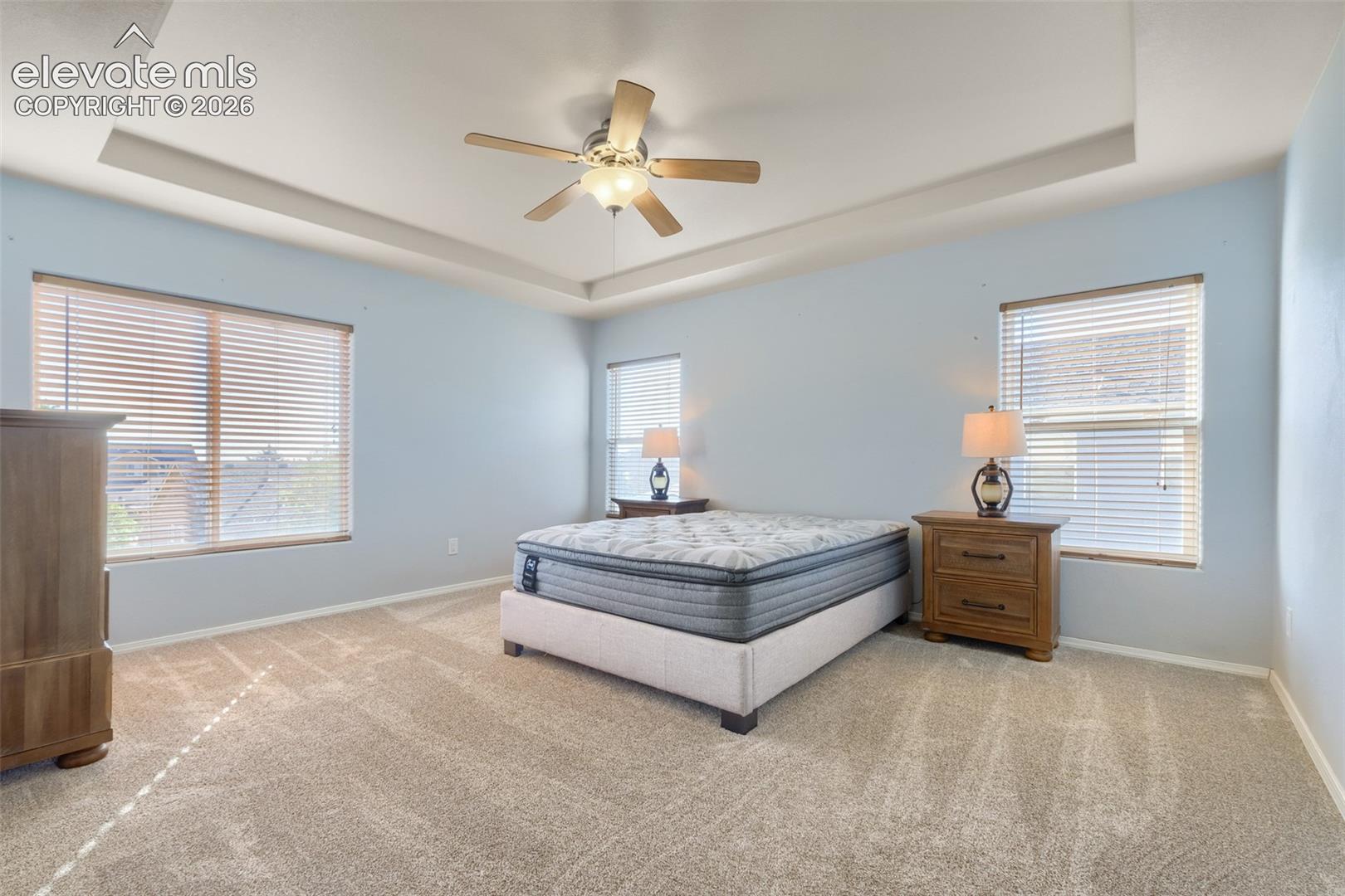 Master bedroom with recessed ceiling with a central ceiling fan and light fixture