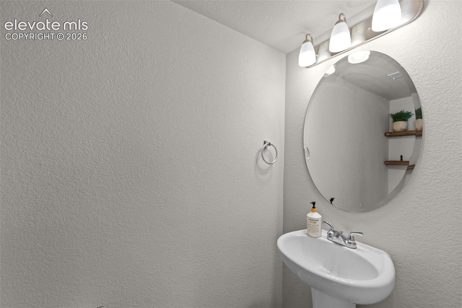 Pedestal sink with chrome faucet, oval mirror, and wall-mounted light fixture