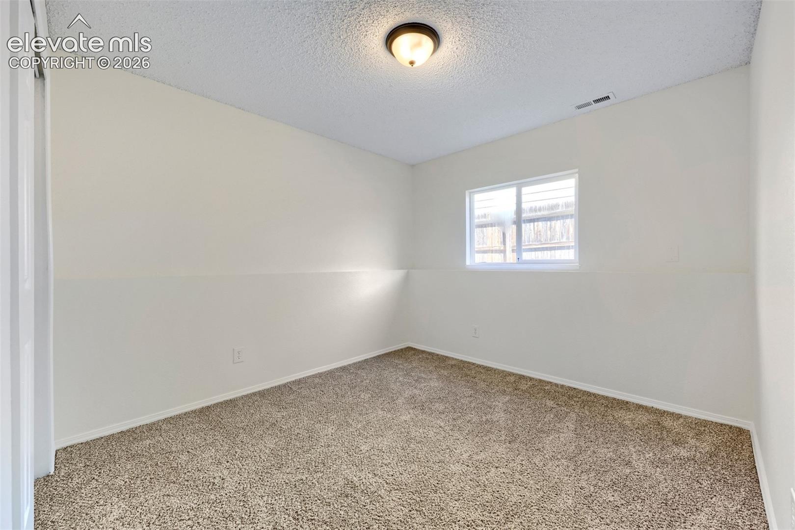 Neutral wall tones with a textured ceiling, carpeted flooring, and a single window