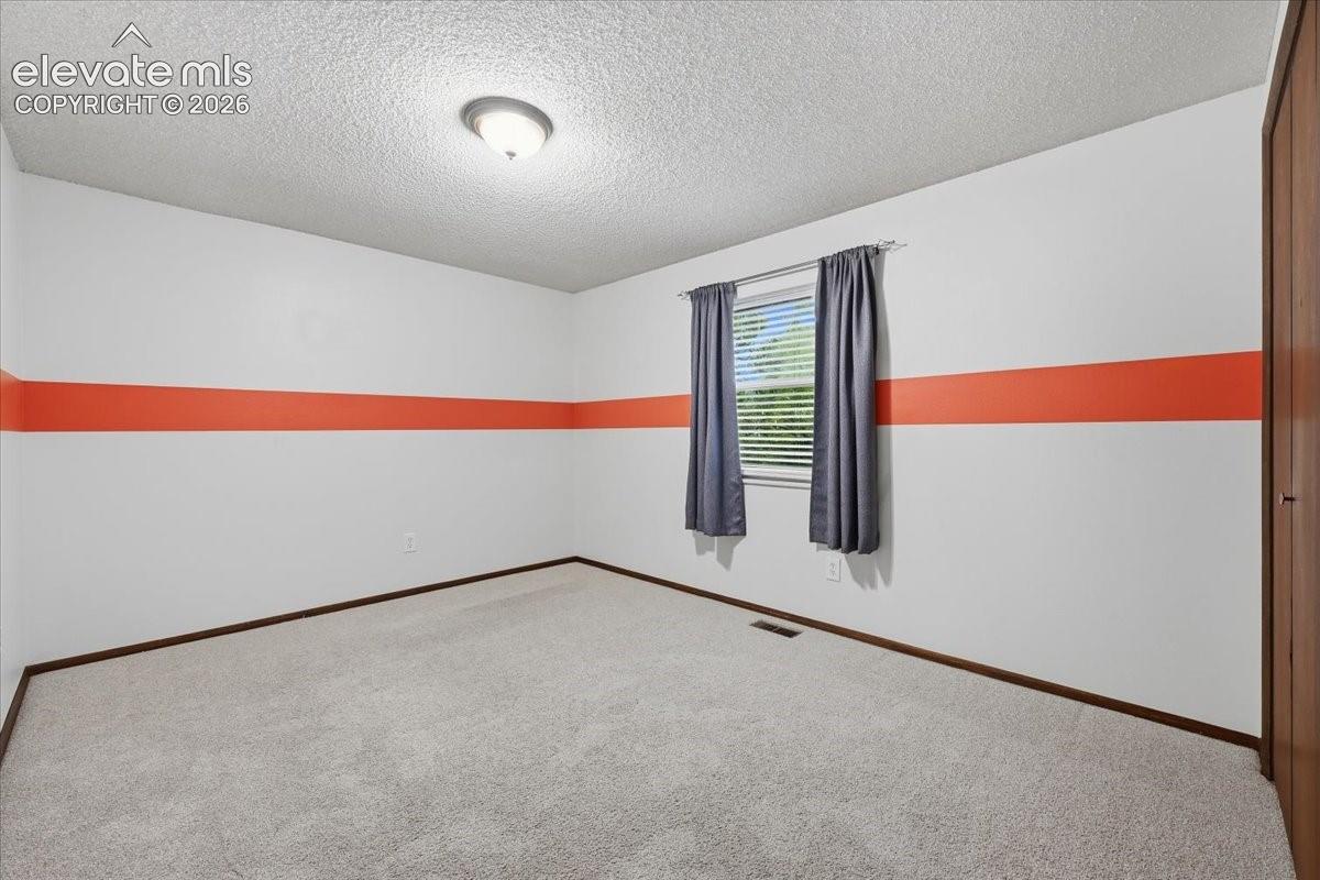 Bedroom 2 with overhead lighting, blinds and a window overlooking the backyard