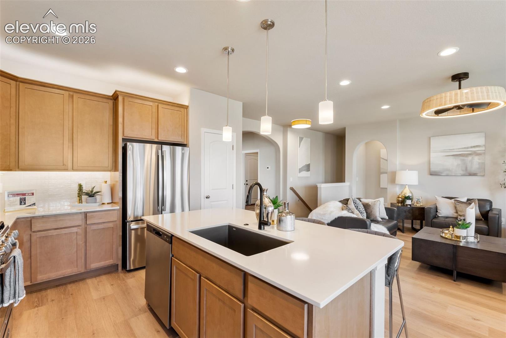 Kitchen featuring light-finish cabinetry, a central island with a quartz countertop, an undermount sink, matte black plumbing fixtures, and wood-finish flooring