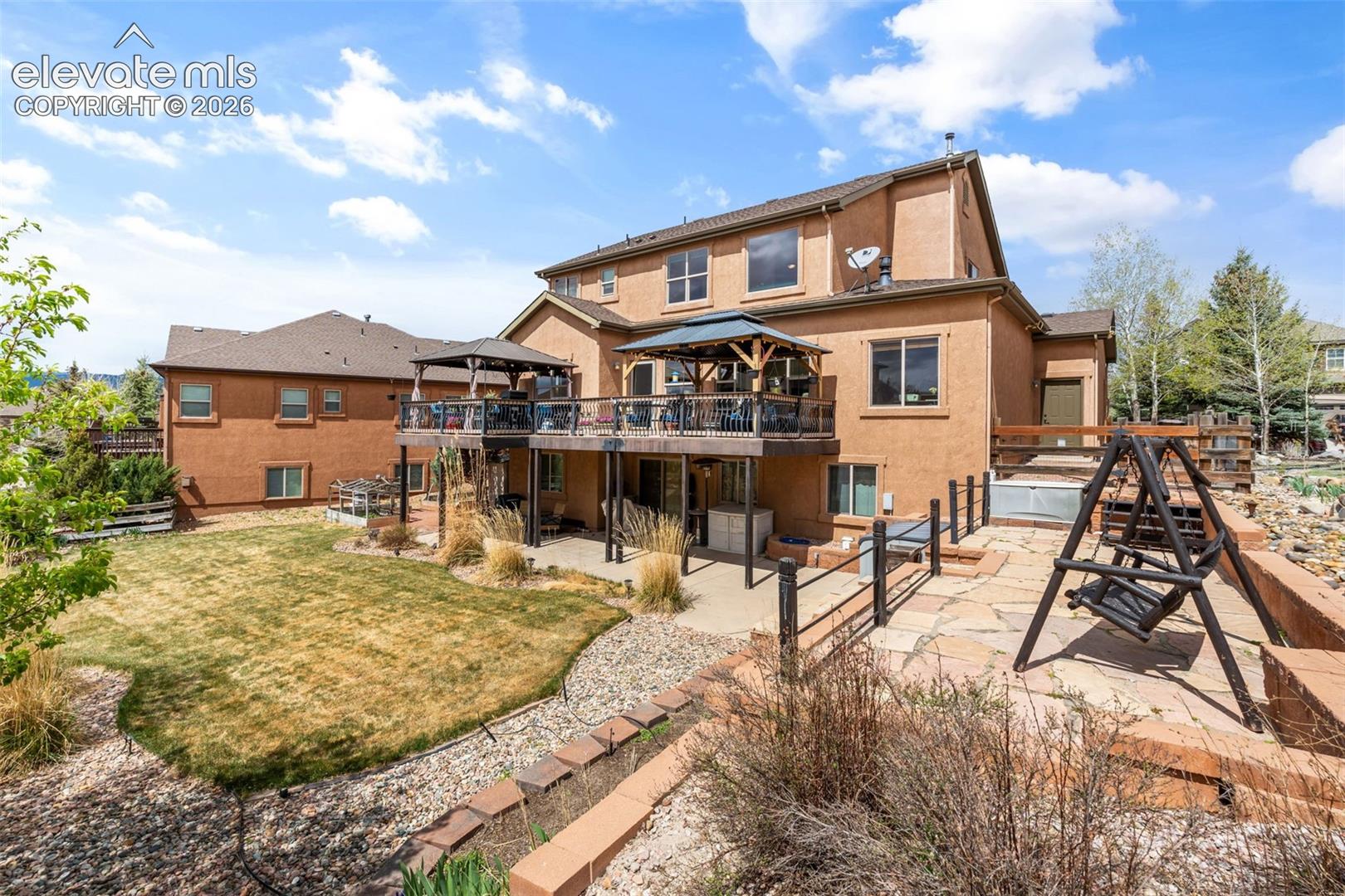 Multi-level rear exterior featuring a deck with a built-in gazebo, lower-level patio with flagstone, and a grassed yard area