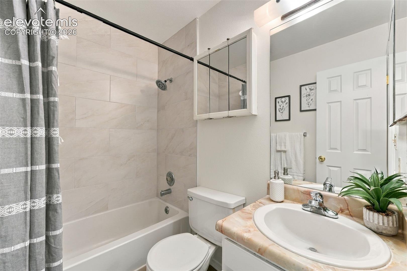 Bathroom featuring a tiled tub surround, integrated medicine cabinet, vanity with a stone-finish countertop, and wall-mounted vanity lighting