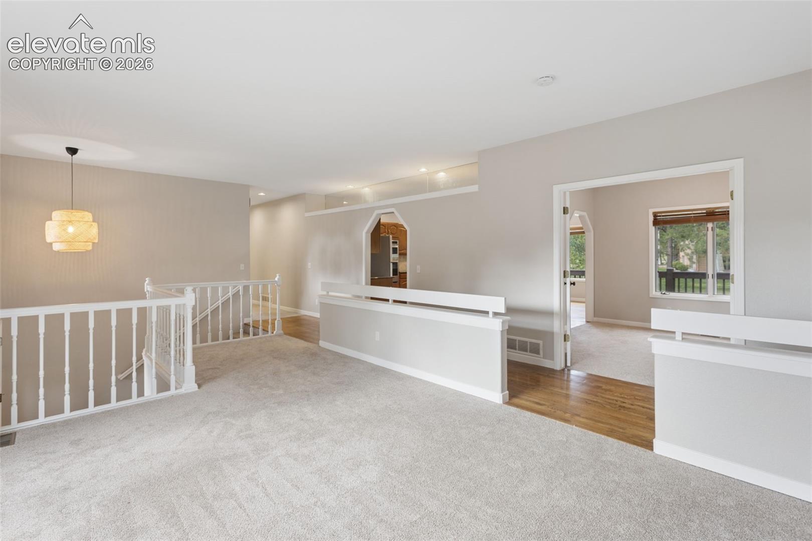 Expansive carpeted area with a decorative pendant light fixture, white banister, wood-finish flooring accents, and arched entryways