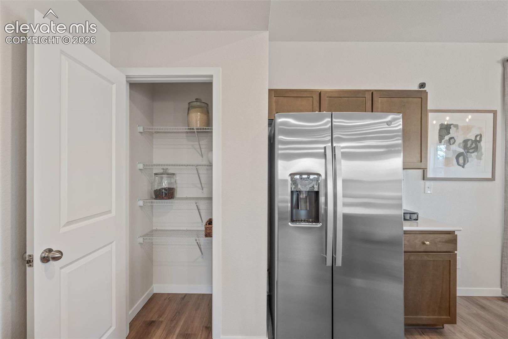 Stainless steel side-by-side refrigerator, wood-finish flooring, and pantry with wire shelving