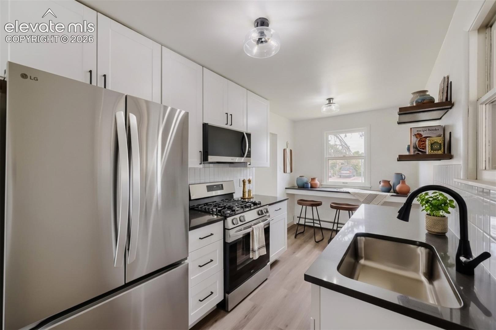 Stainless steel refrigerator, gas range with oven, built-in microwave, white shaker-style cabinetry, and wood-finish flooring