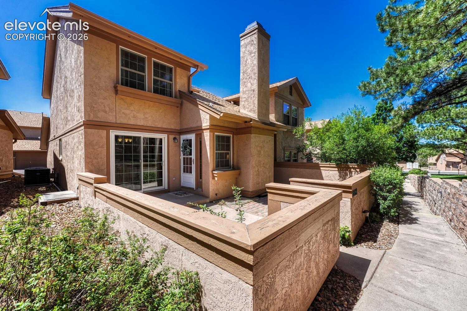 Front of home with enclosed courtyard, surrounded by peaceful, lush green spaces, mature trees, and shrubs.