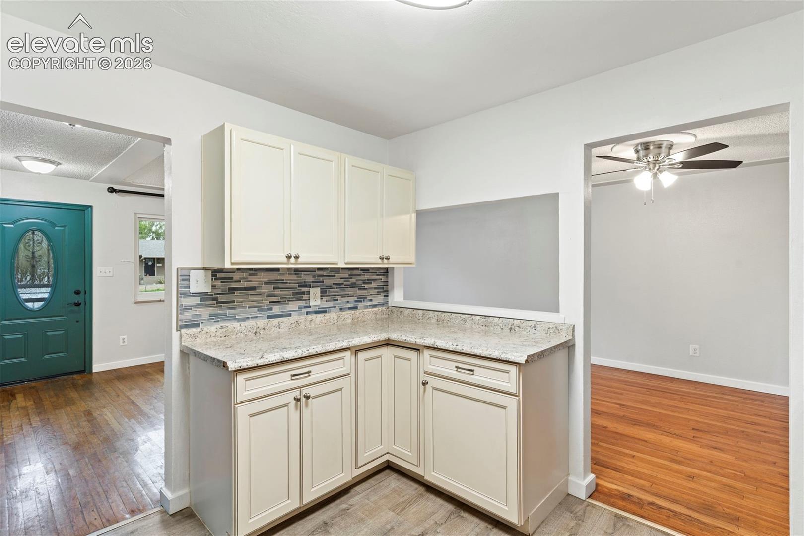 Cream-toned cabinetry with dark hardware, speckled countertops, and a mosaic tile backsplash