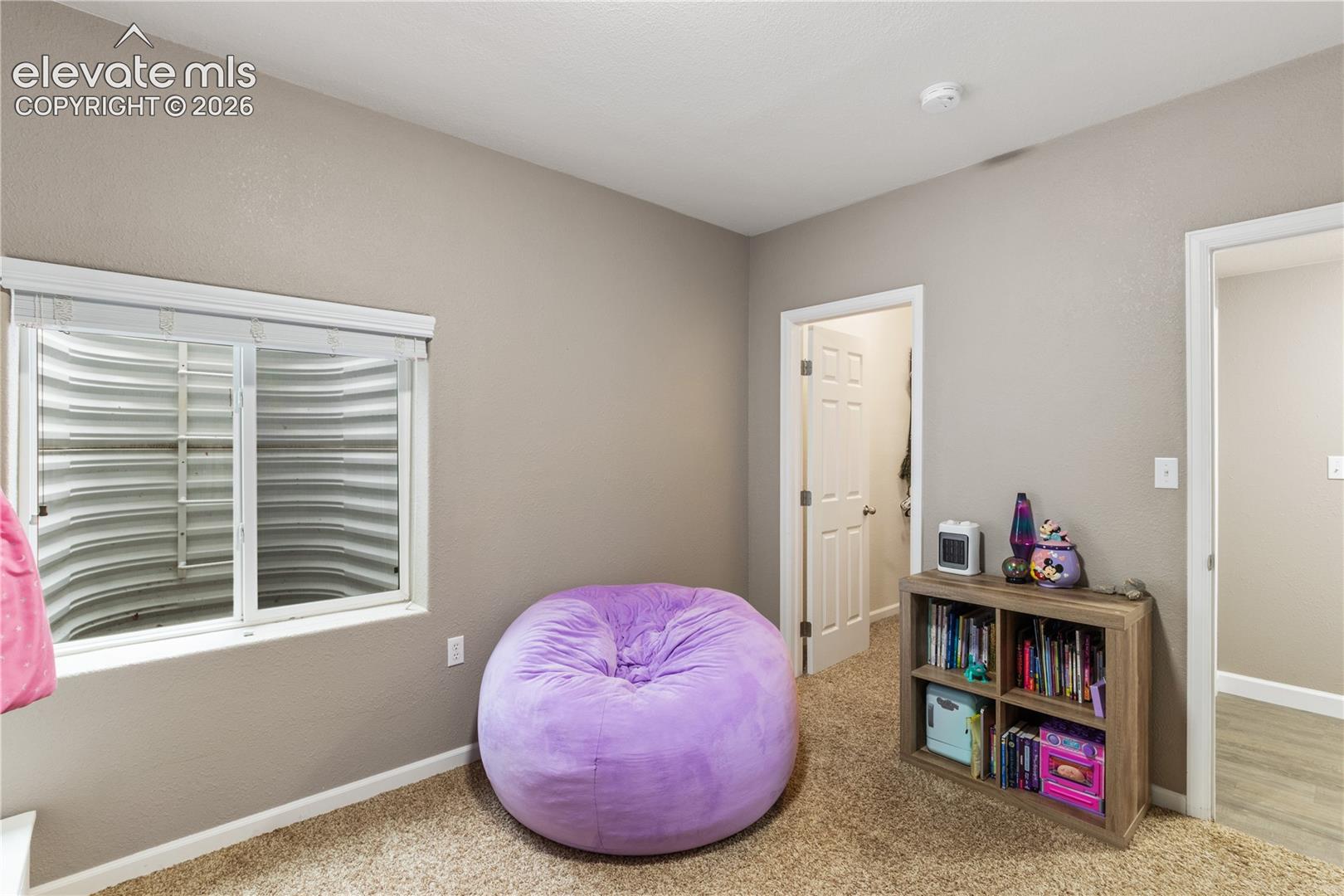 Neutral-toned interior space featuring carpeting, a sliding window with an integrated egress well, and a white paneled door