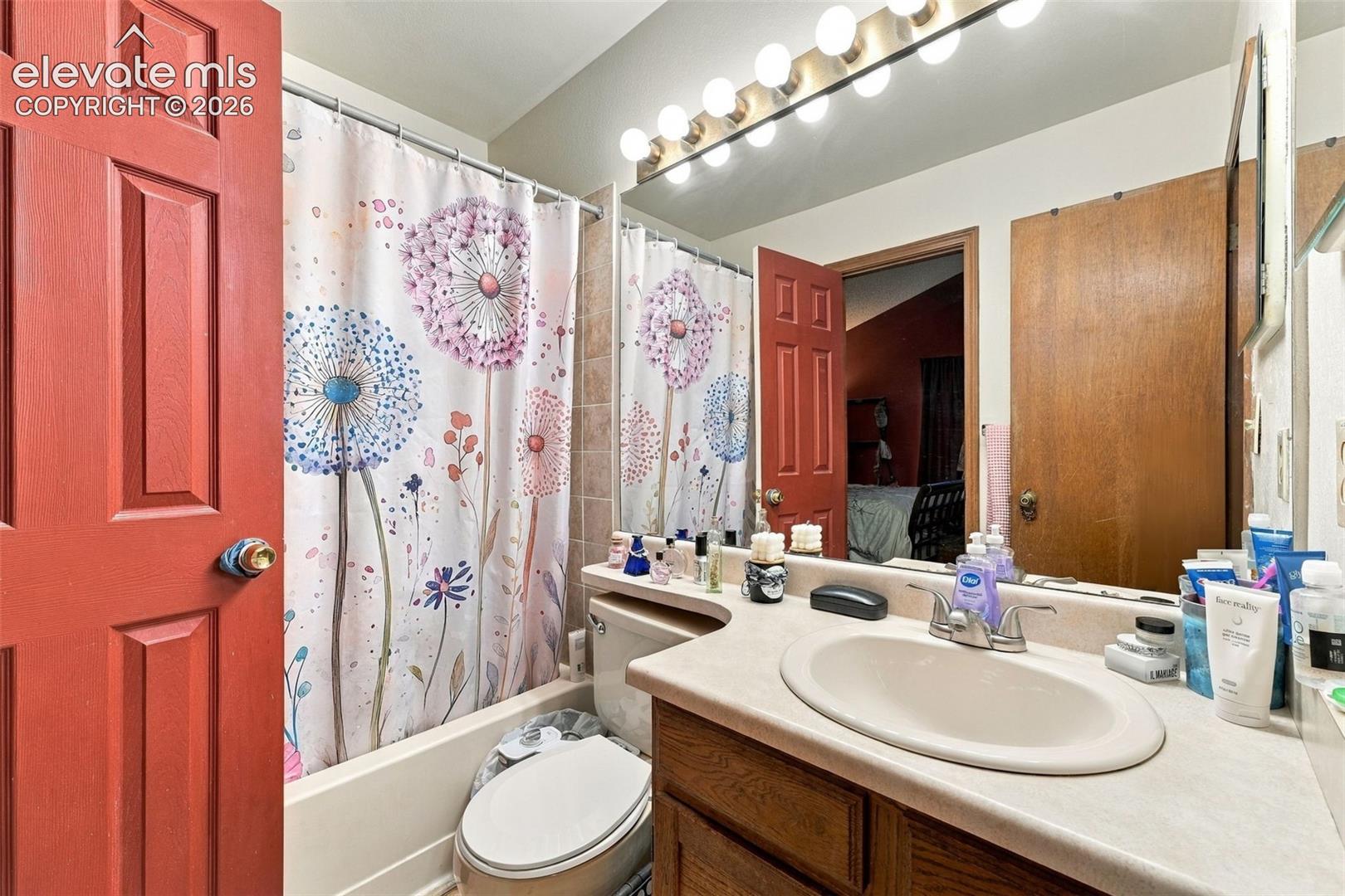 Bathroom featuring a wood-finish vanity with a molded countertop and integrated sink, a full-width vanity mirror, a multi-bulb light fixture, and a tile-surround tub